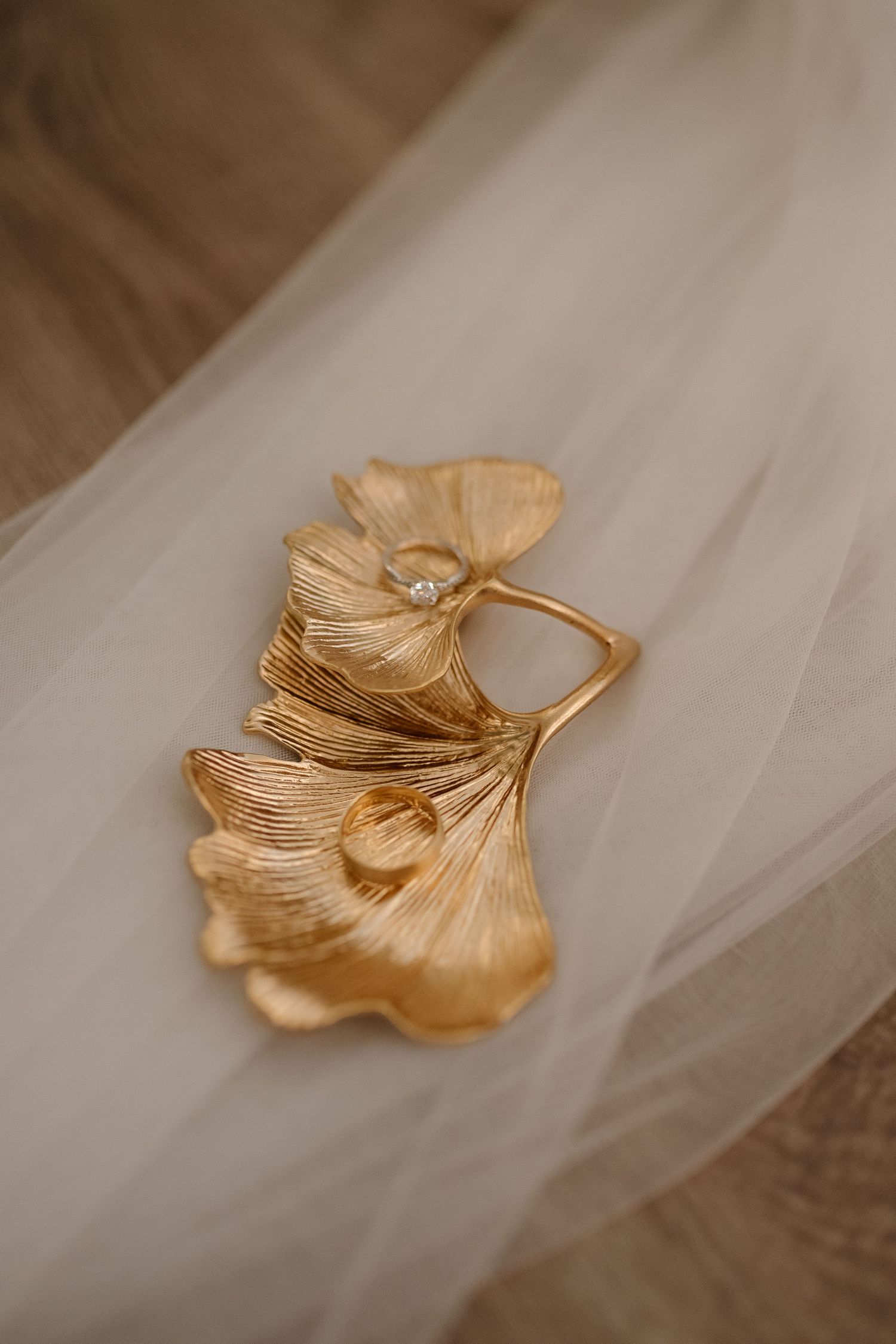 Gold metallic leaf-shaped decorative pin laying on delicate white tulle fabric.
