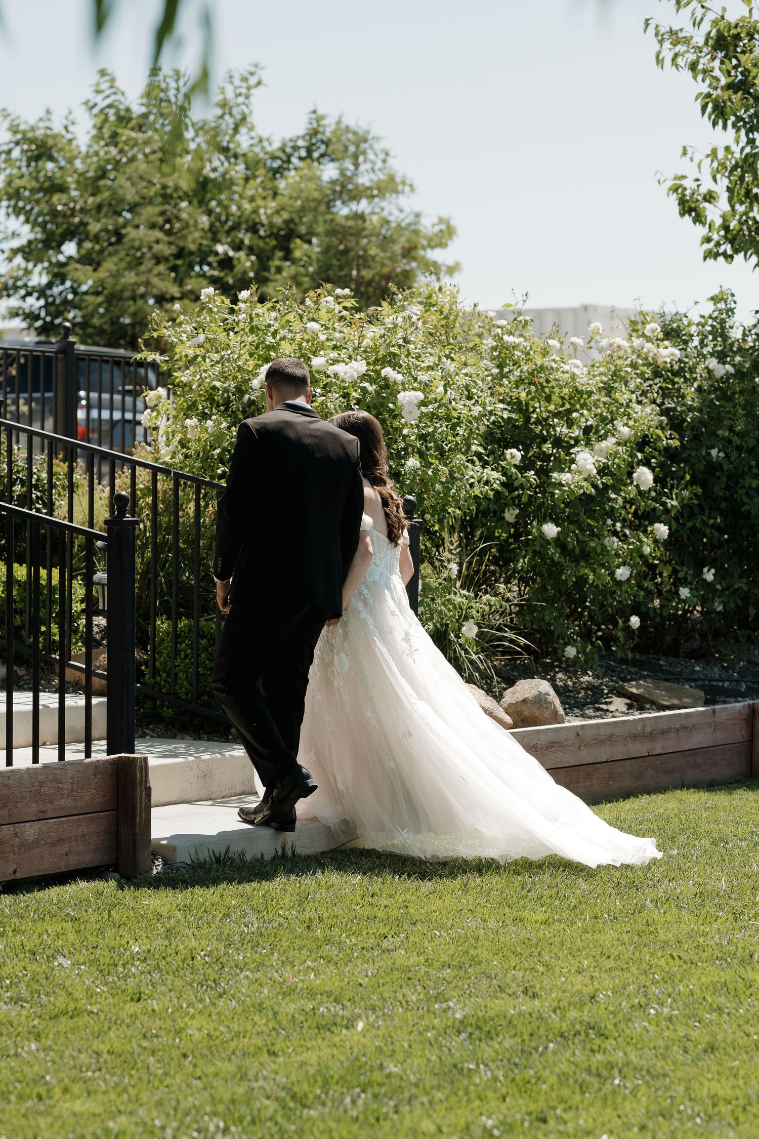 A couple shares an intimate moment in a garden setting with white railings and lush greenery.