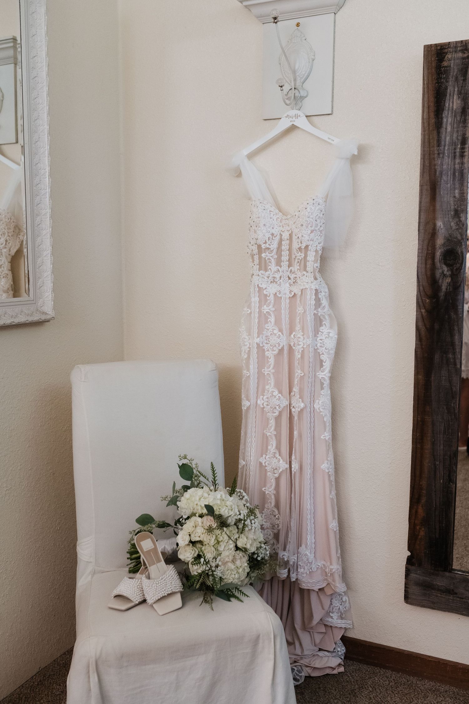 Delicate blush lace wedding dress displayed on white hangers in a bridal suite.