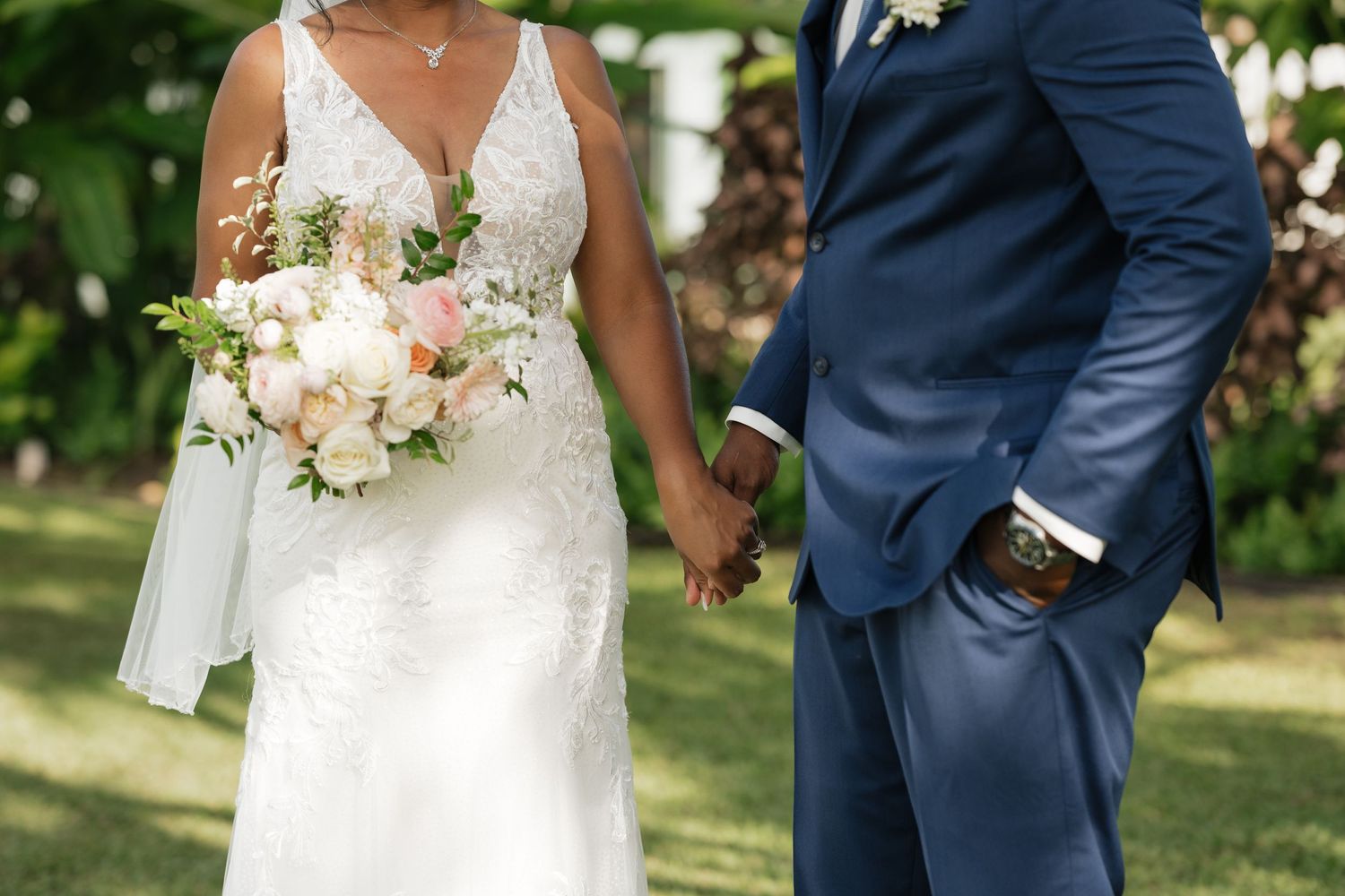 Elegant wedding couple poses among trees while holding a pastel floral bouquet.