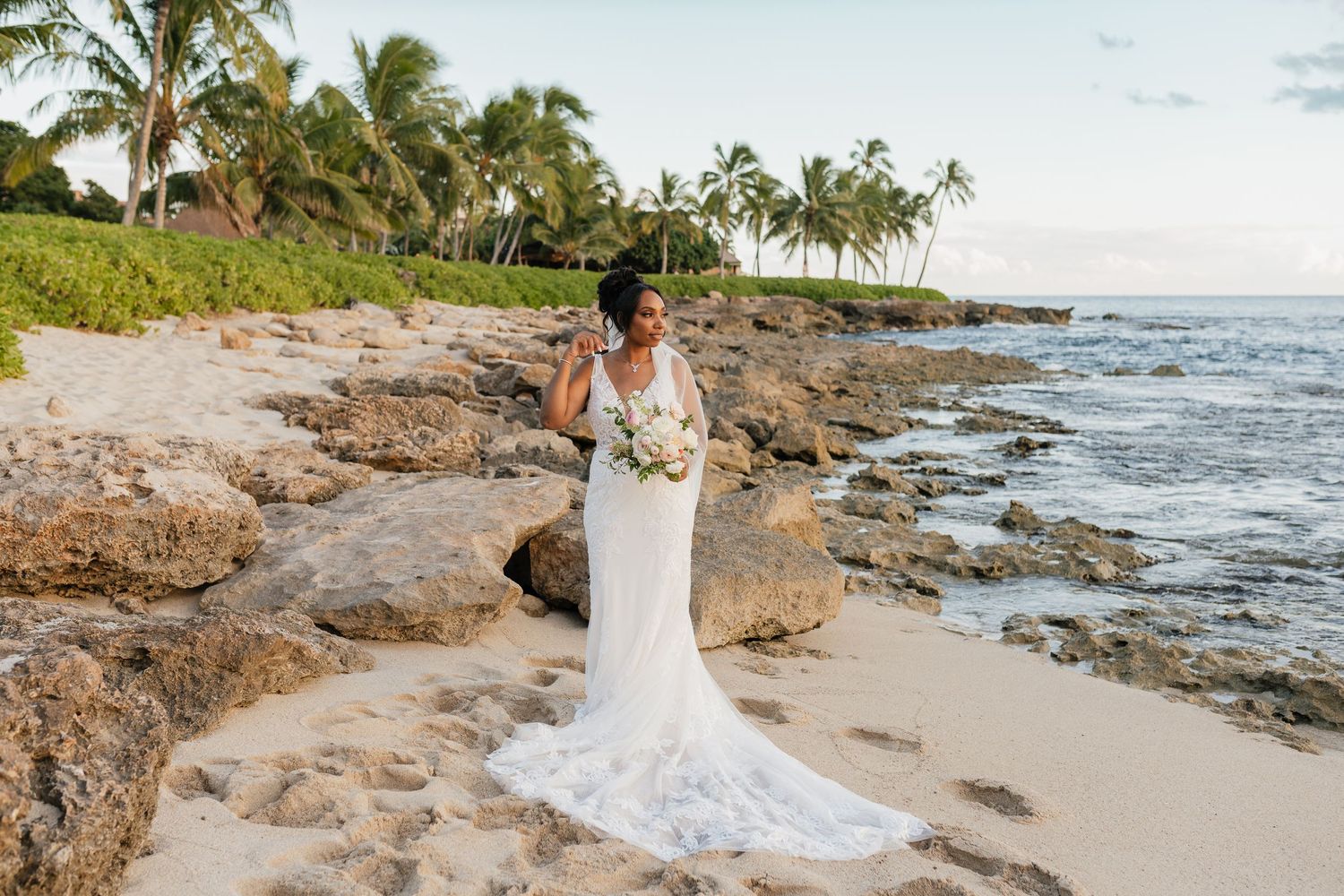 Tropical beach wedding photography with palm trees and rocky shoreline.