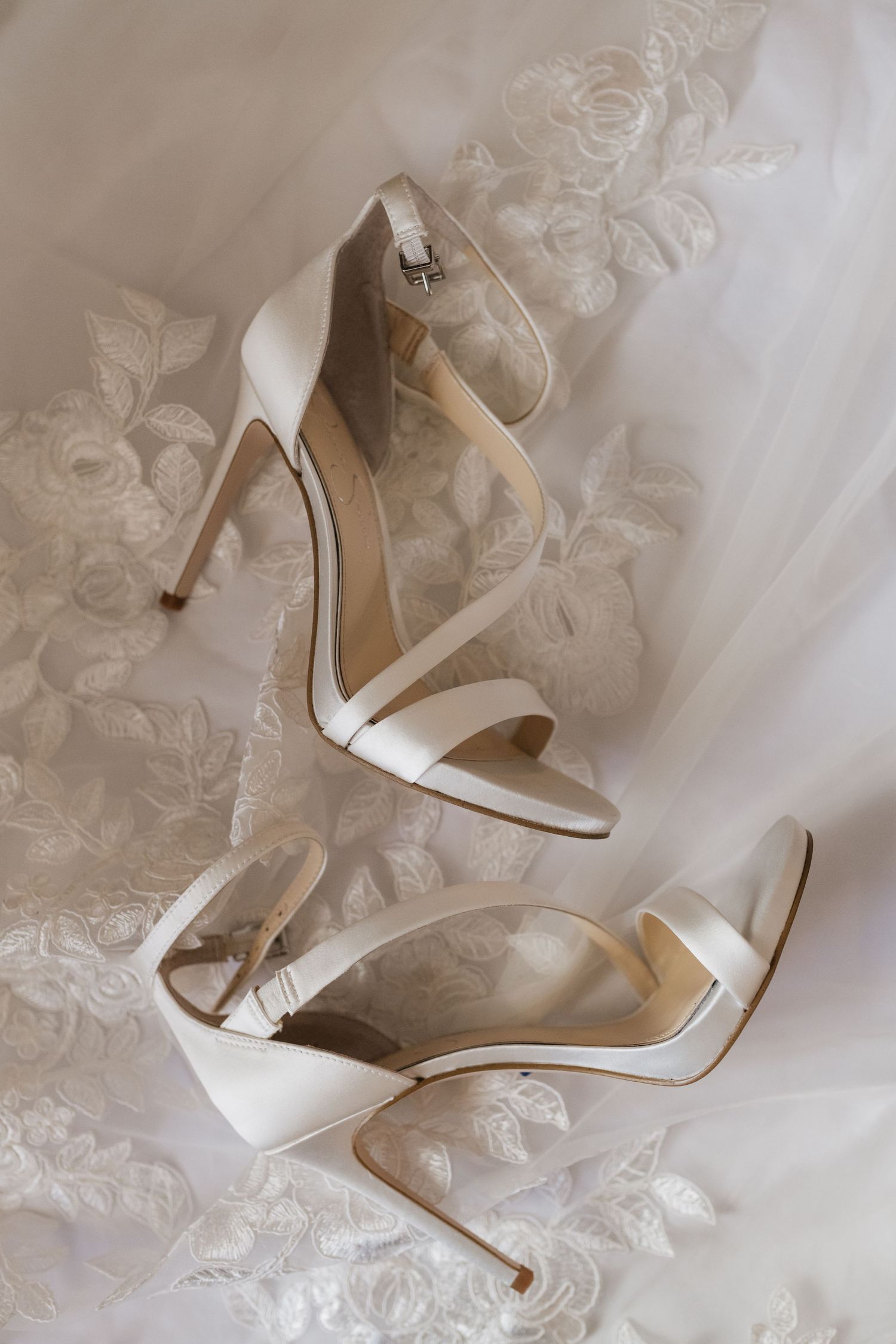 Elegant white bridal heels displayed on delicate lace fabric.