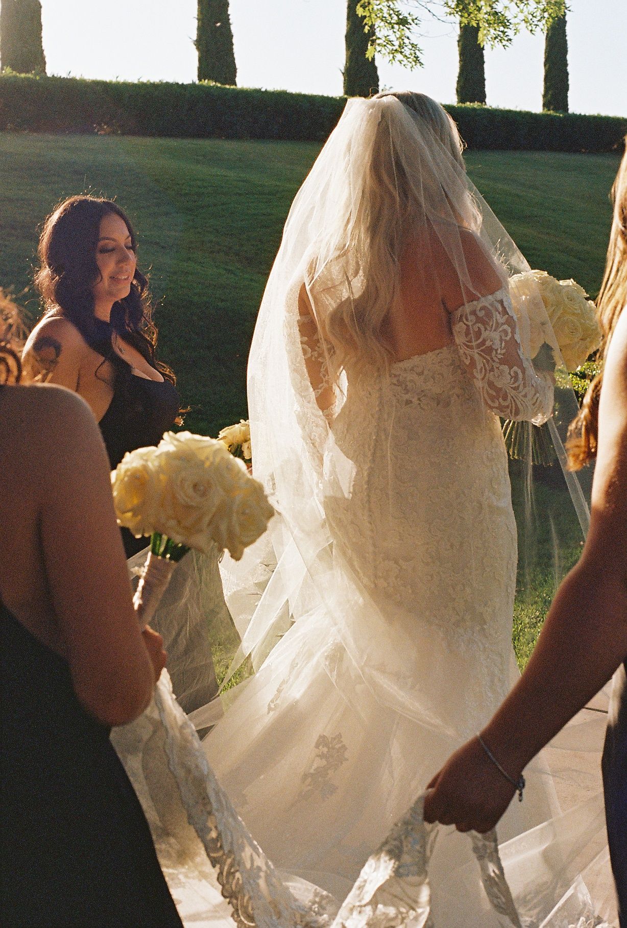 Wedding party walking along pathway with flowing white wedding dress trailing behind.