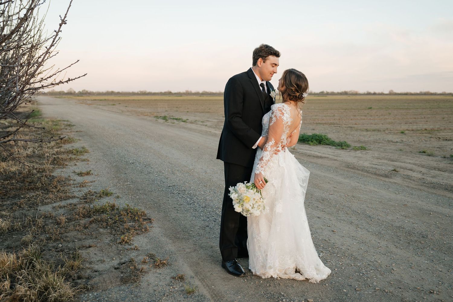 Newlyweds share romantic moments at sunset on a rustic dirt path.