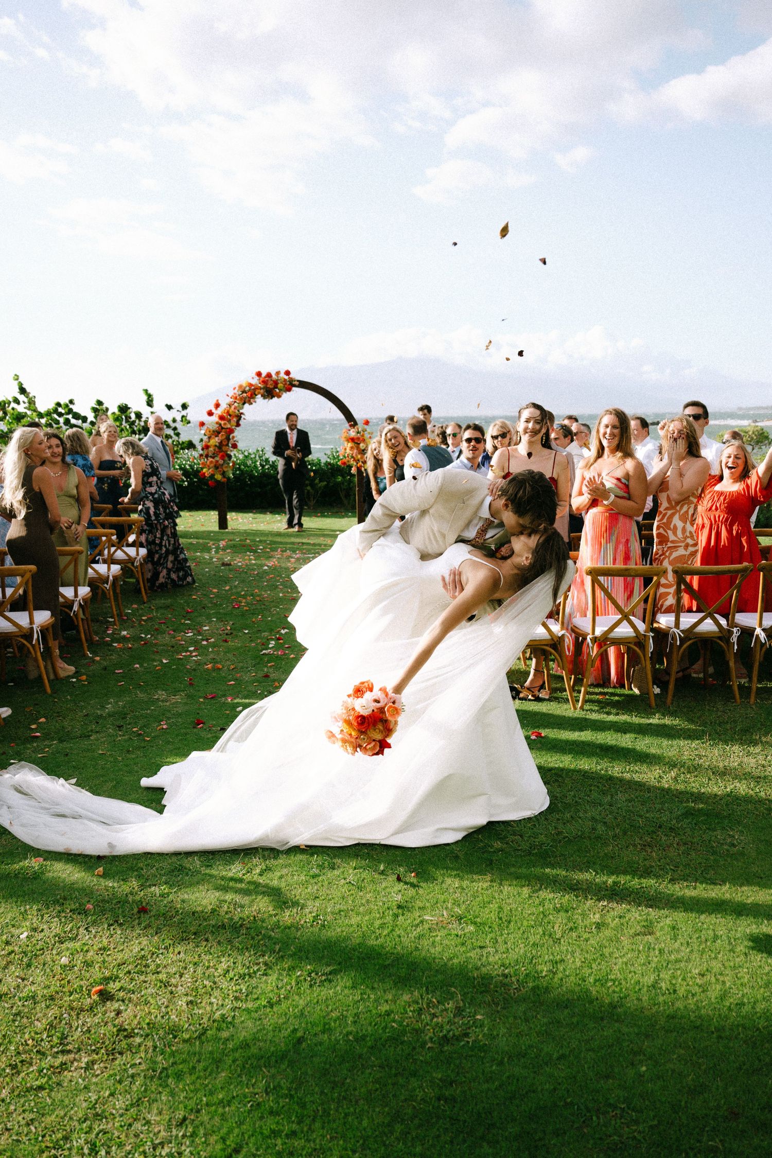 Wedding ceremony on a grassy hilltop with guests watching the bride's veil flowing in the wind.