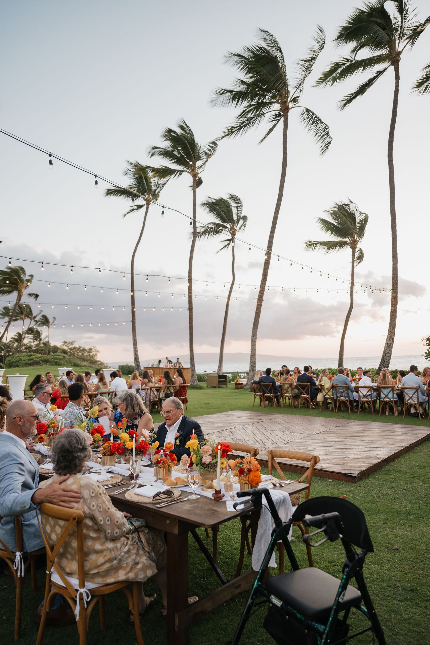 Outdoor wedding reception under string lights with palm trees swaying in the breeze at sunset.