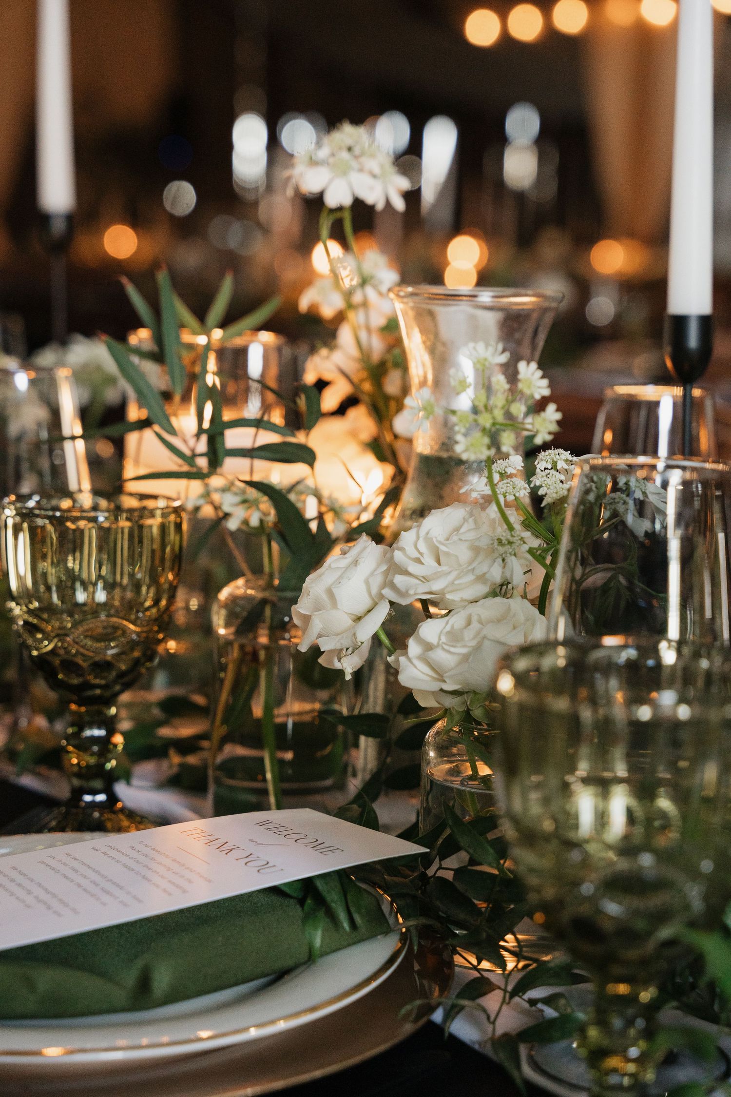 Intimate table settings with white roses, candles and greenery create an elegant wedding reception atmosphere.