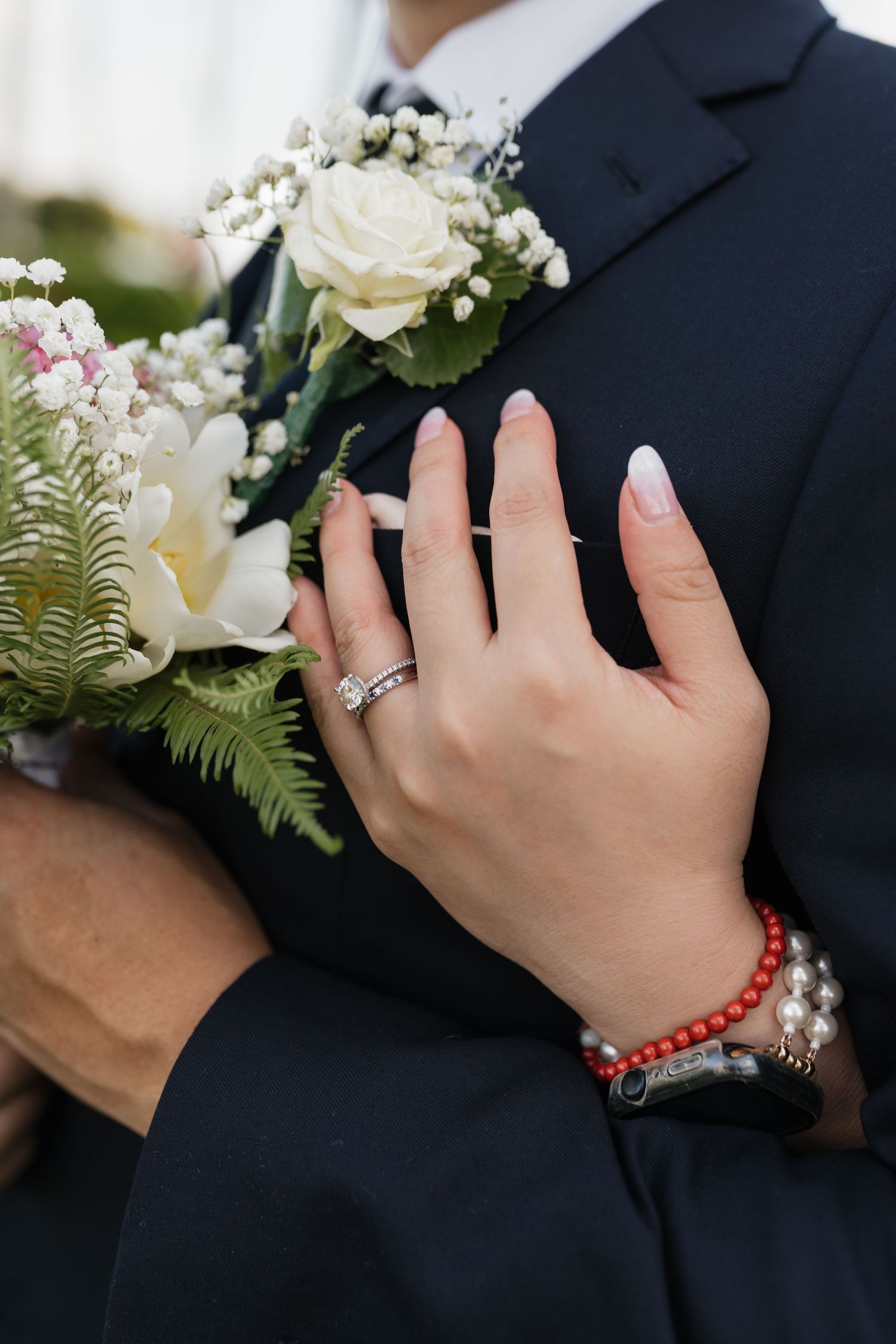 Close-up of hands wearing wedding rings with white floral bouquet details.