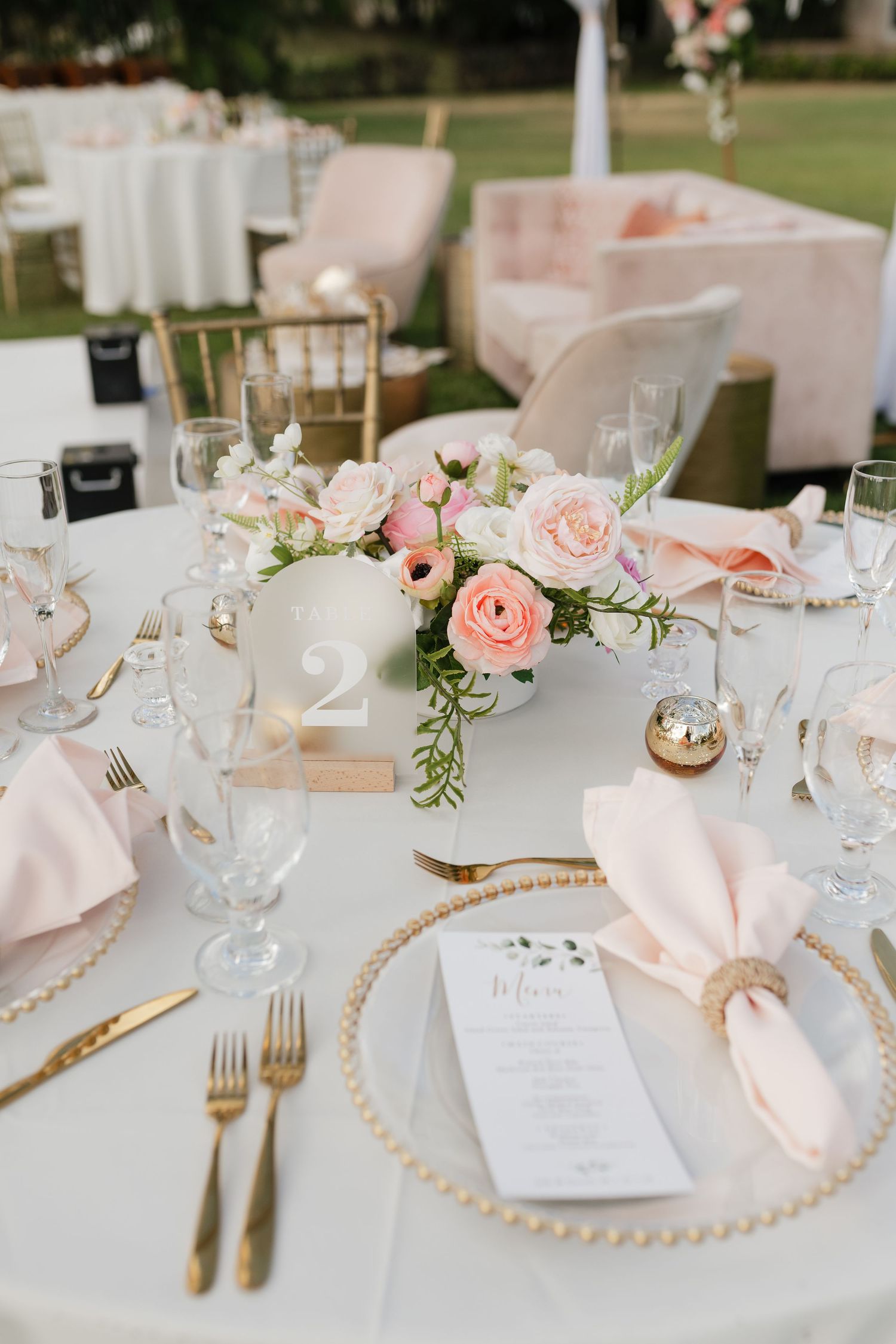 Wedding reception table setting with pink napkins, pearl chargers, and blush floral centerpieces.
