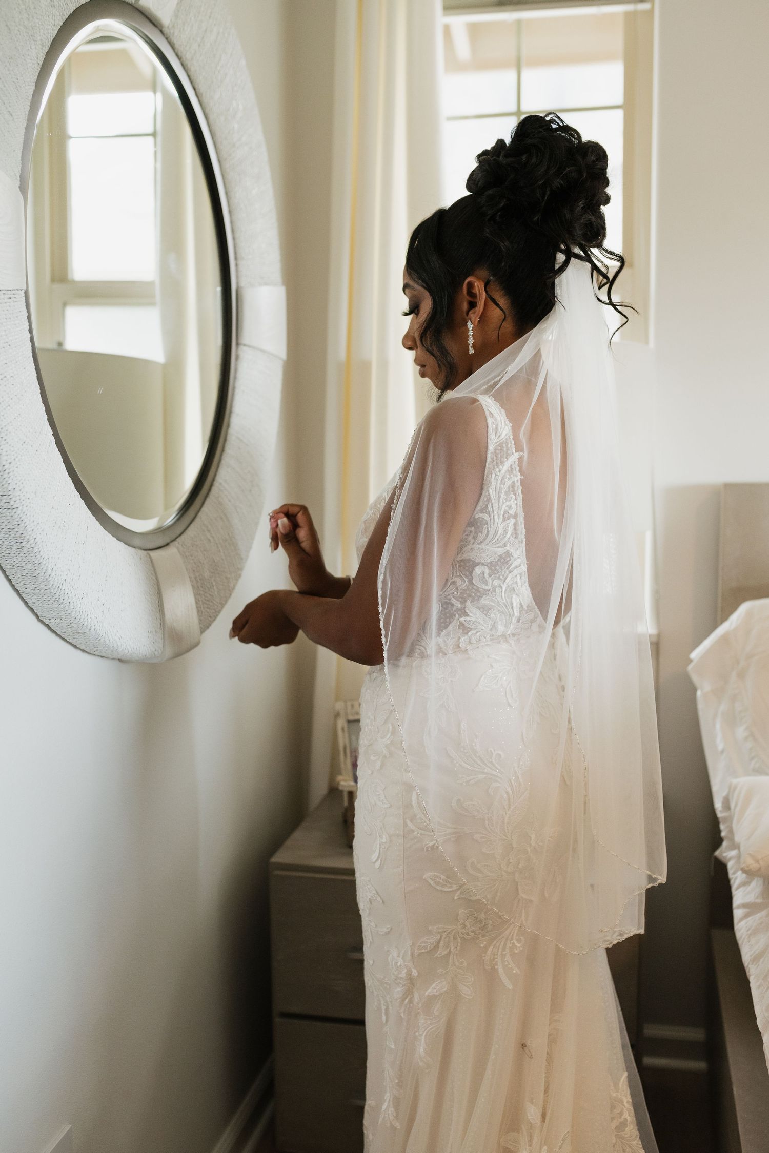 A series of intimate getting ready moments showing a bride in her white lace wedding dress looking in mirrors.