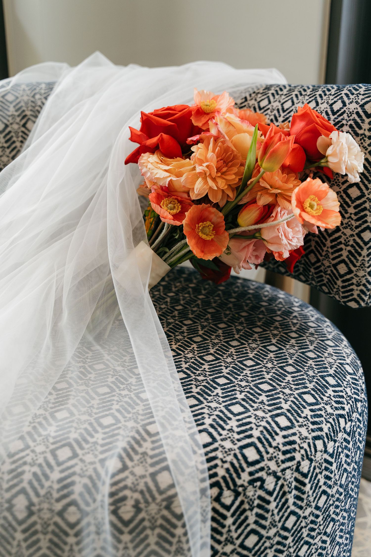 Coral-colored carnations rest atop a black and white geometric patterned surface with flowing white tulle fabric.