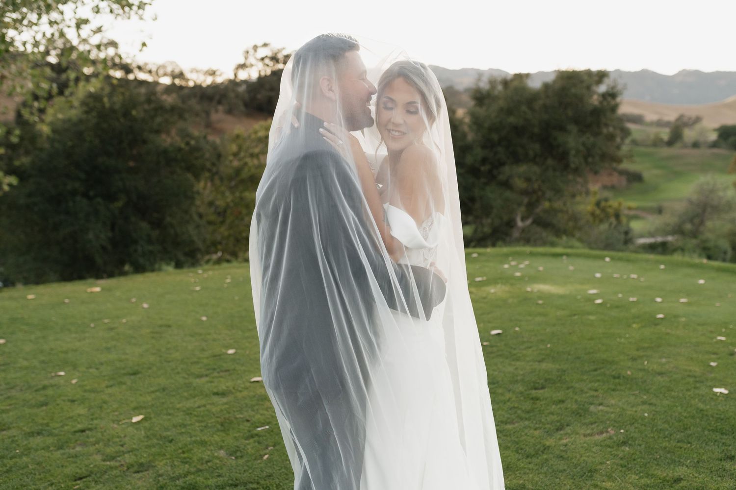 Bride in flowing veil stands gracefully against scenic mountain backdrop.