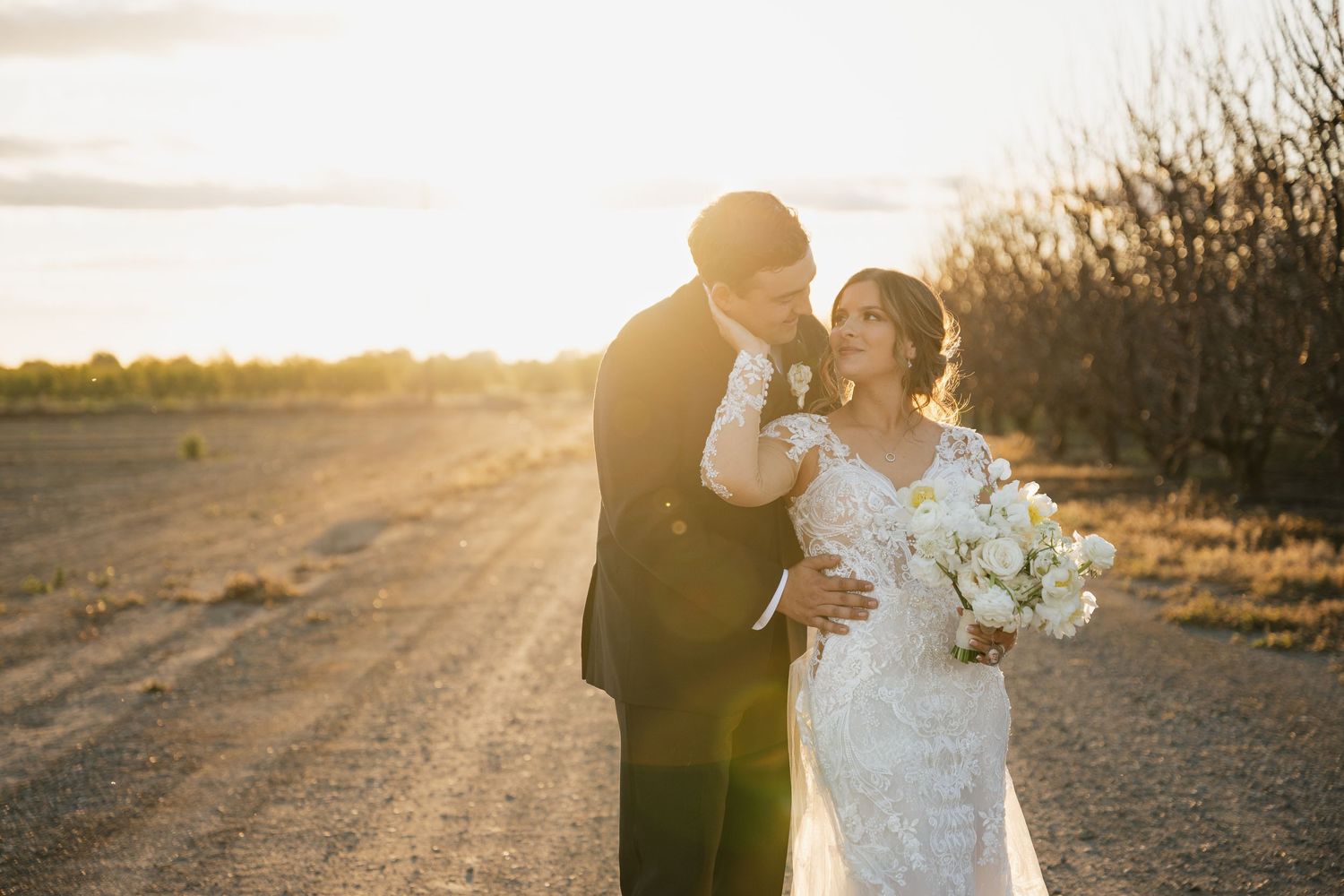 Sunlit wedding portrait on country road with dramatic golden hour lighting.