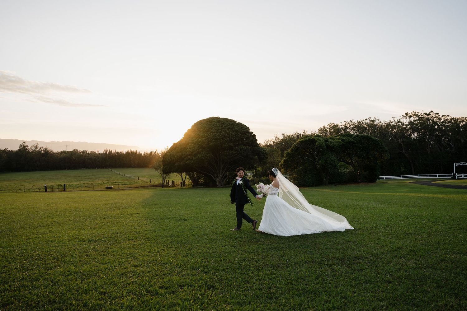 A bride and groom dance on a lush green lawn at sunset, with her white gown flowing in the breeze.