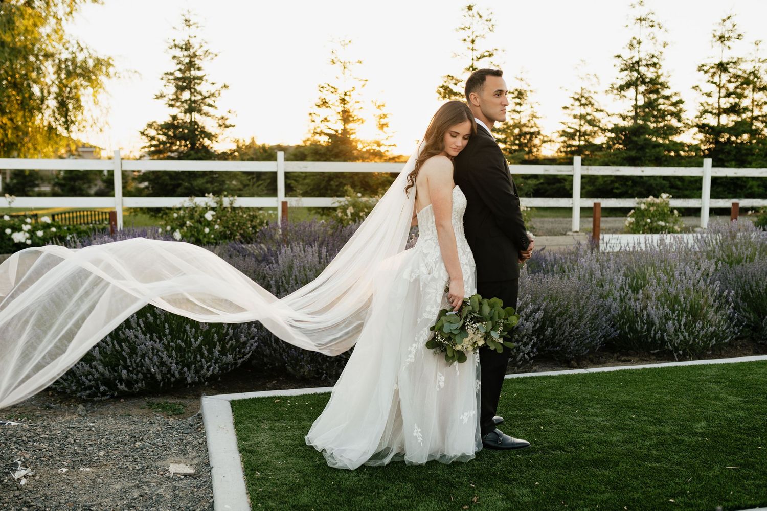 A dramatic wedding photo with the bride's veil flowing in the wind against a sunset backdrop.