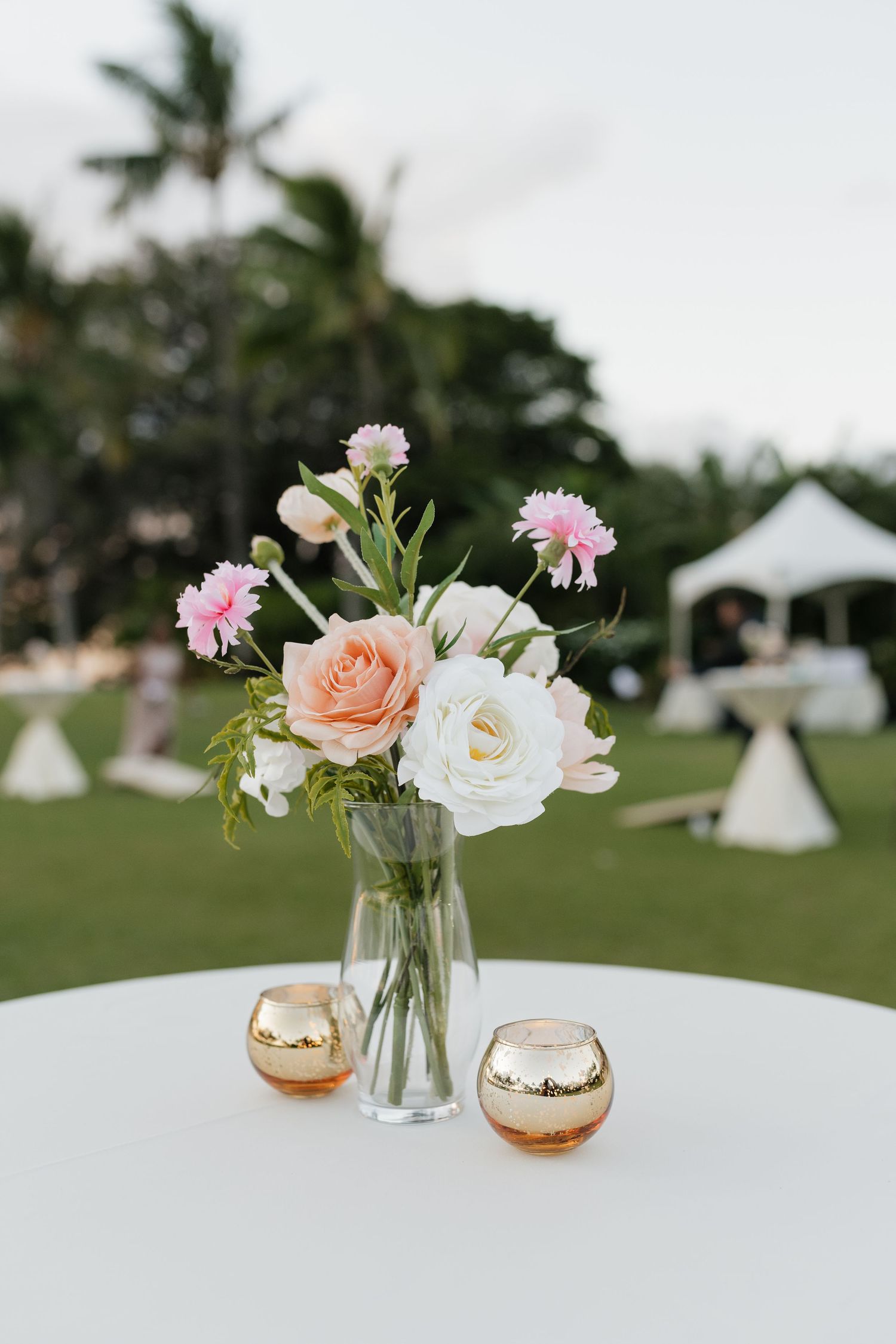 Delicate pink and white flowers in glass vases with gold accents on white table settings.
