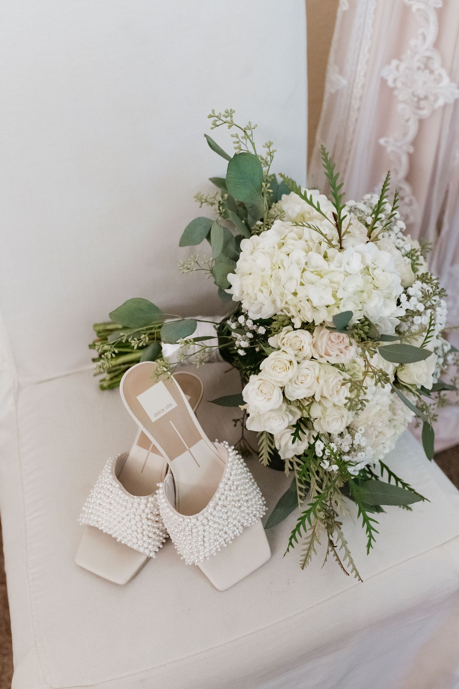 Bridal details featuring pearl-studded wedding shoes next to white hydrangea and eucalyptus bouquet.