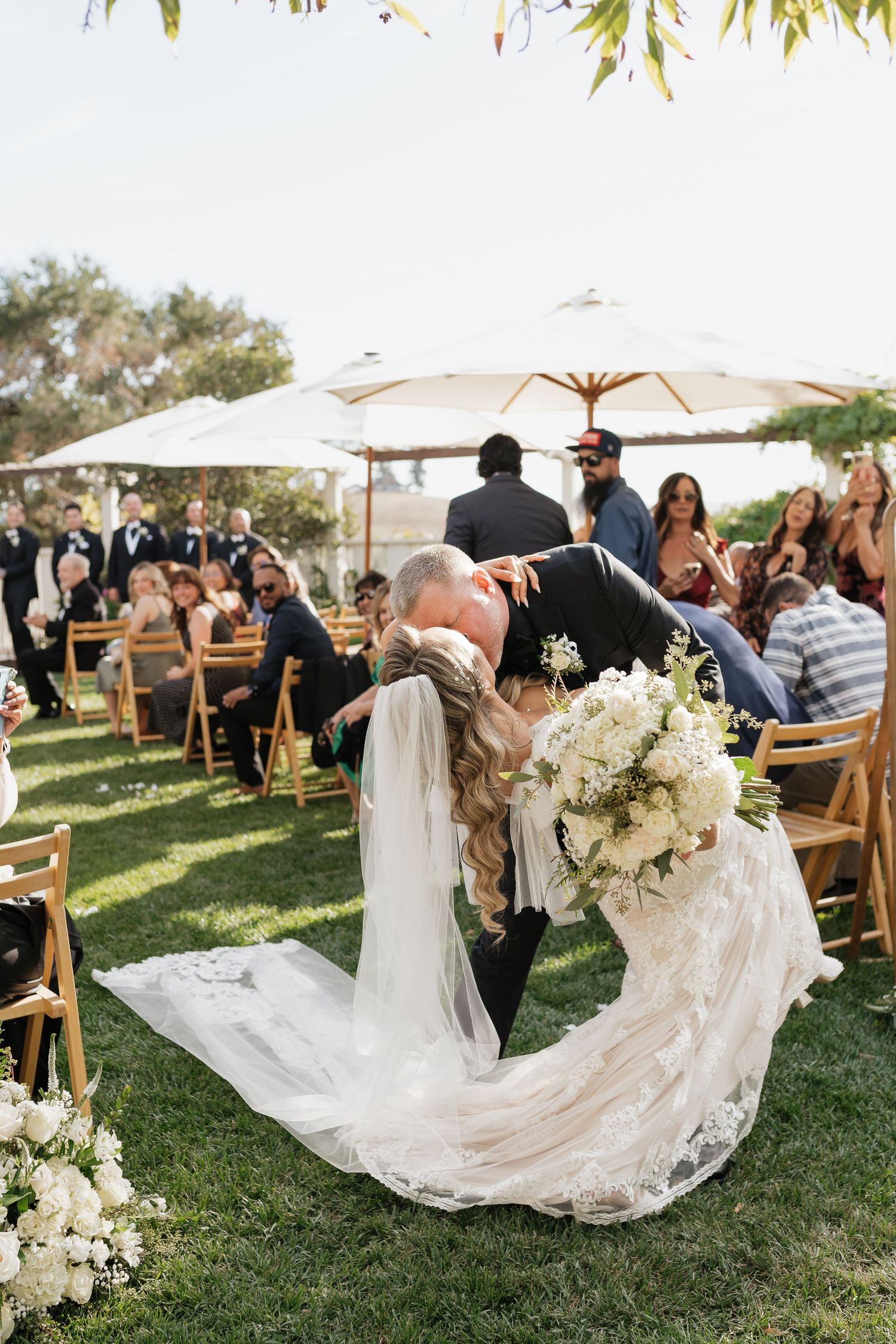 Wedding ceremony taking place on a grassy lawn with white decor and floral arrangements.