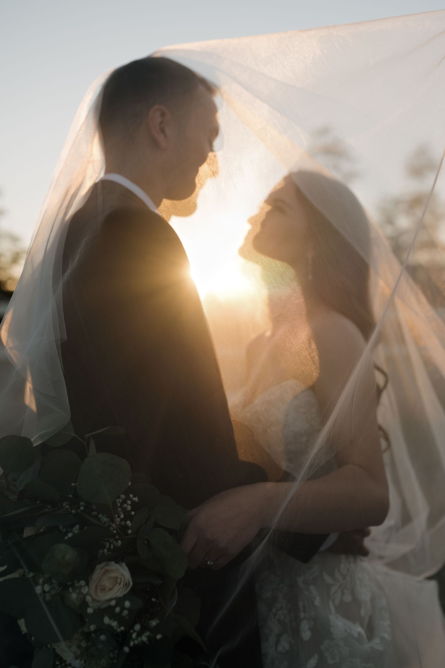 Romantic silhouetted couple embraces under flowing veil at sunset.
