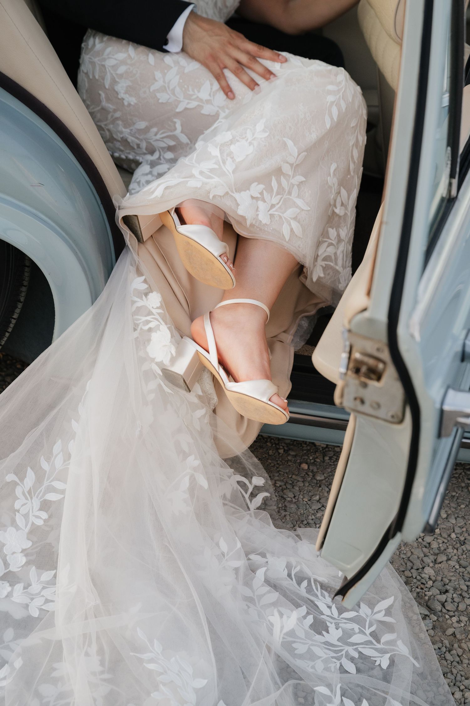 Close-up of bride's feet in elegant heels stepping into classic car with lace dress details.