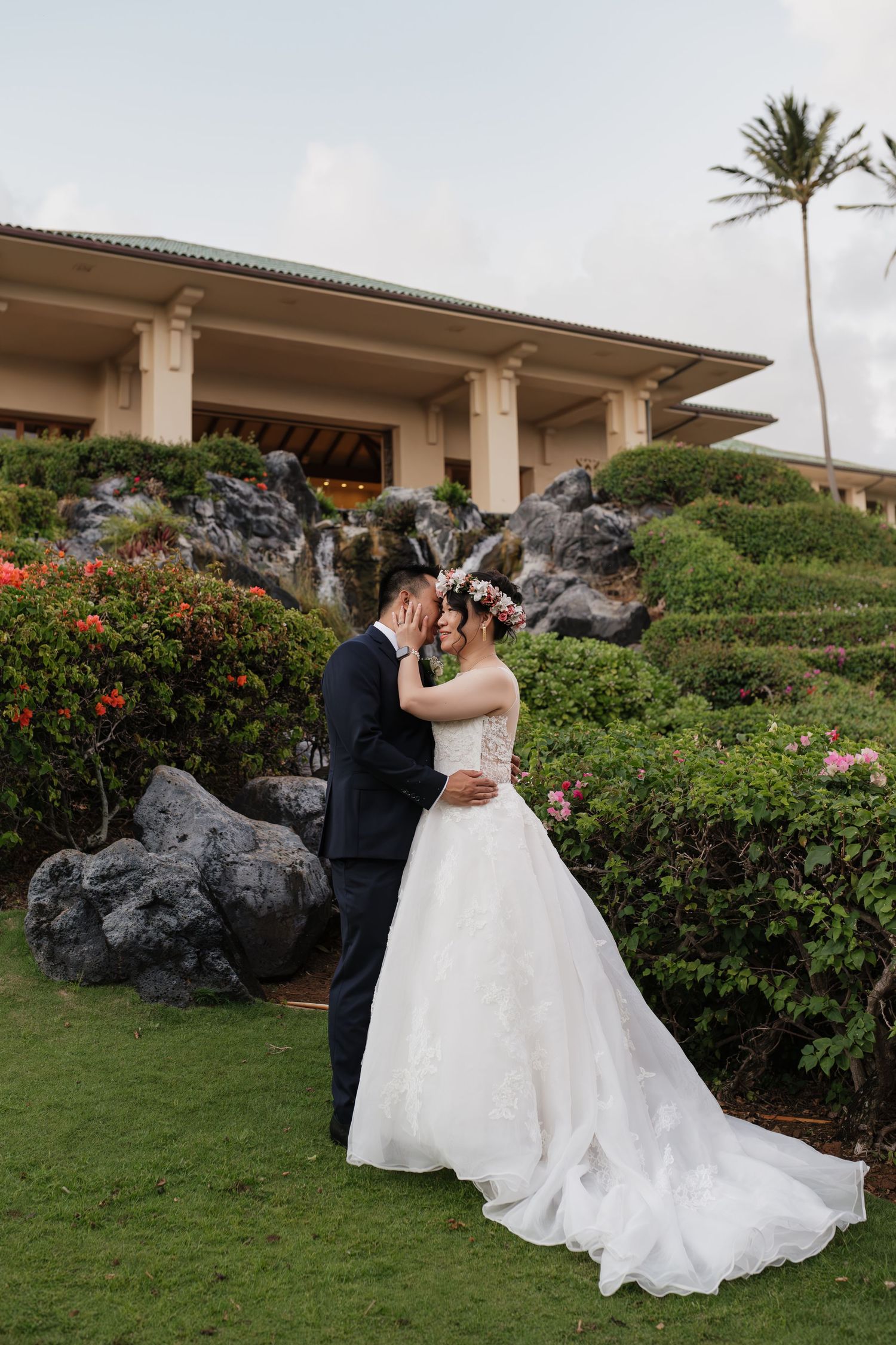 Wedding couple shares romantic moment by tropical landscaping and rock features.