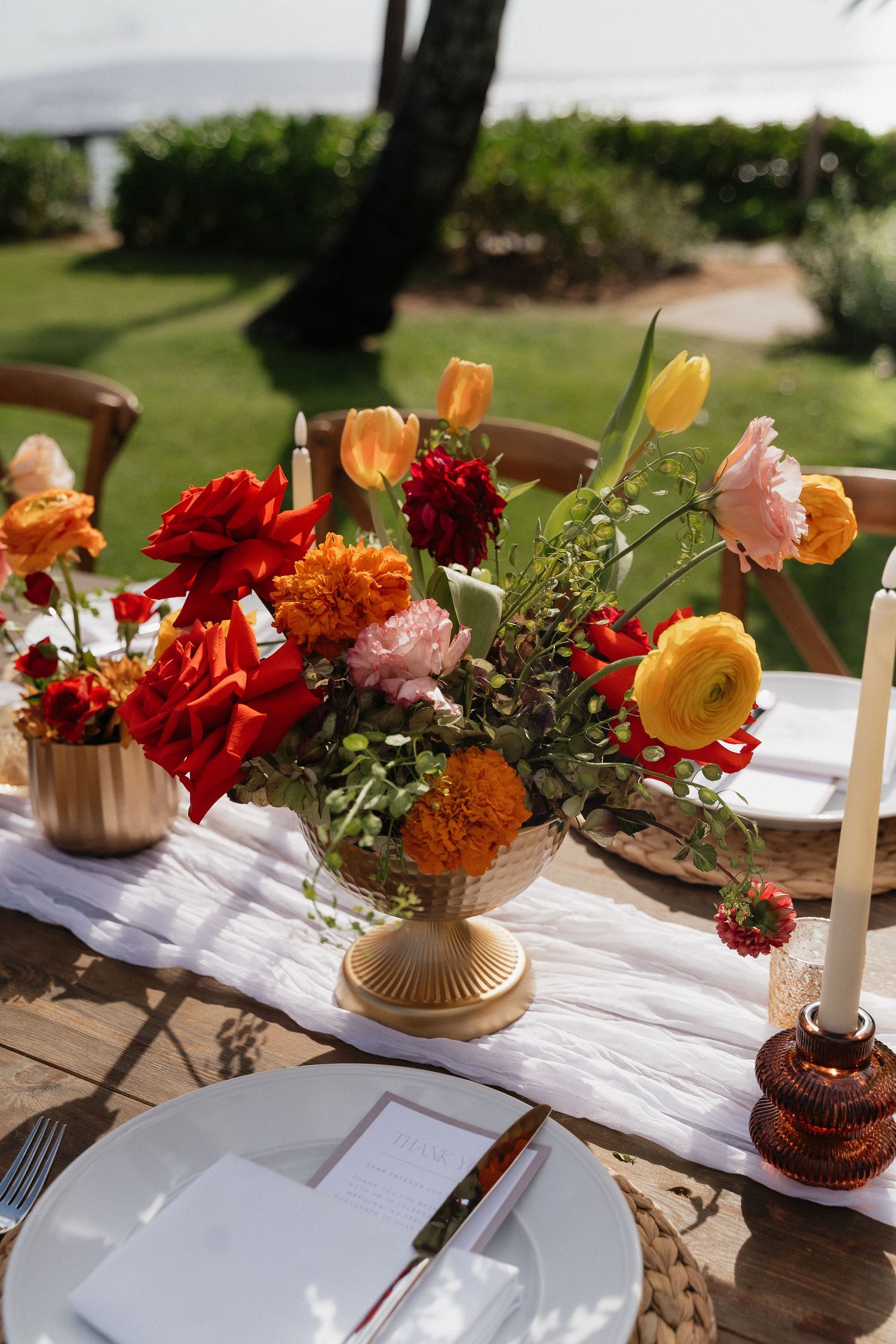 Wedding table setting with colorful floral arrangements in amber and red tones.