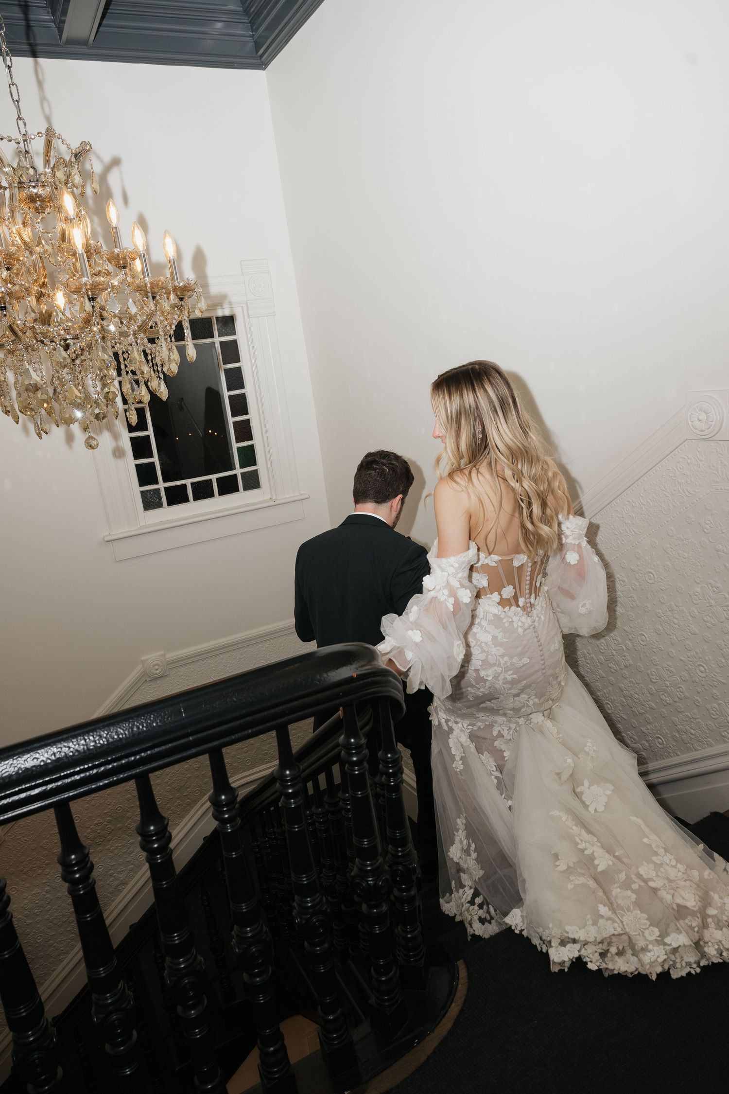 A series of moody wedding photos showing a bride in a lace dress near a crystal chandelier and dark staircase.