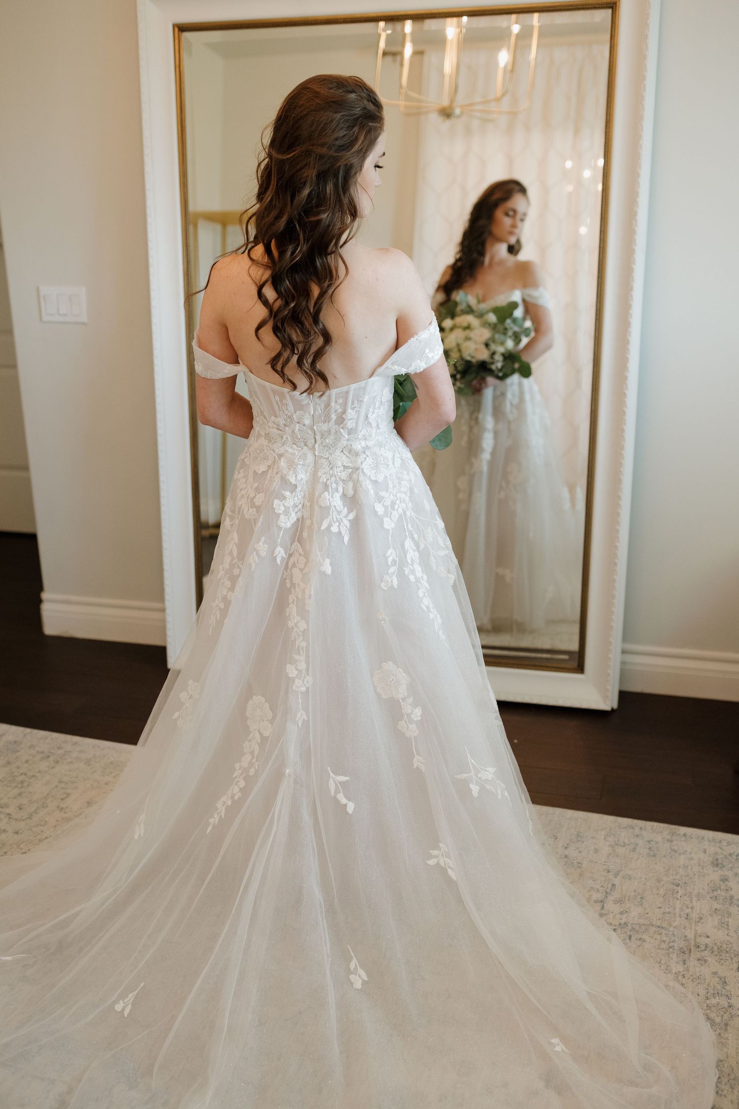 Back view of wedding gown showing intricate lace details and flowing skirt against neutral background.