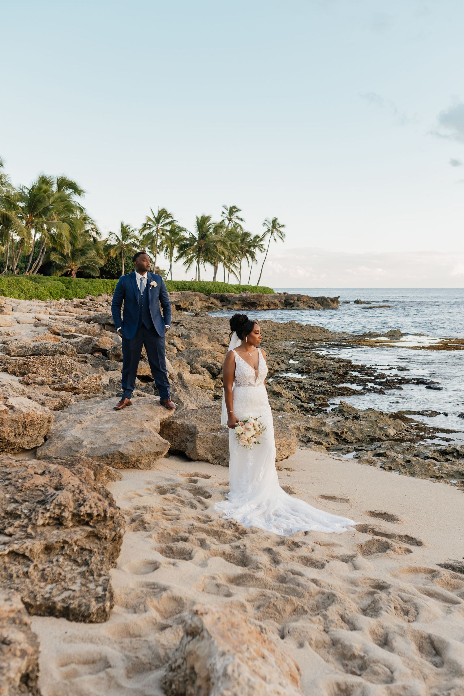 Wedding photography session on sandy beach with volcanic rocks and palm trees.