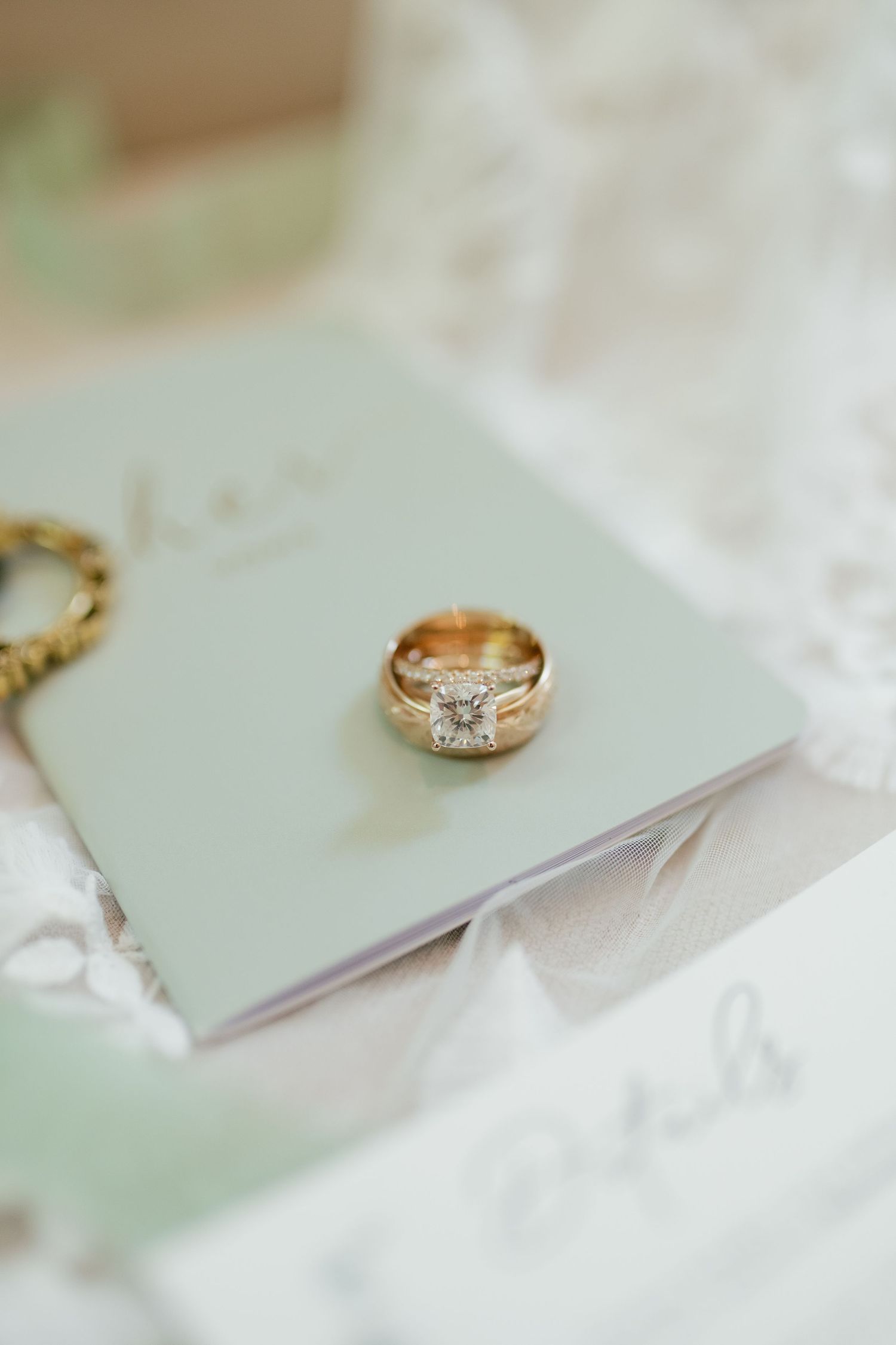 Close-up view of a diamond engagement ring with gold band on mint green background.