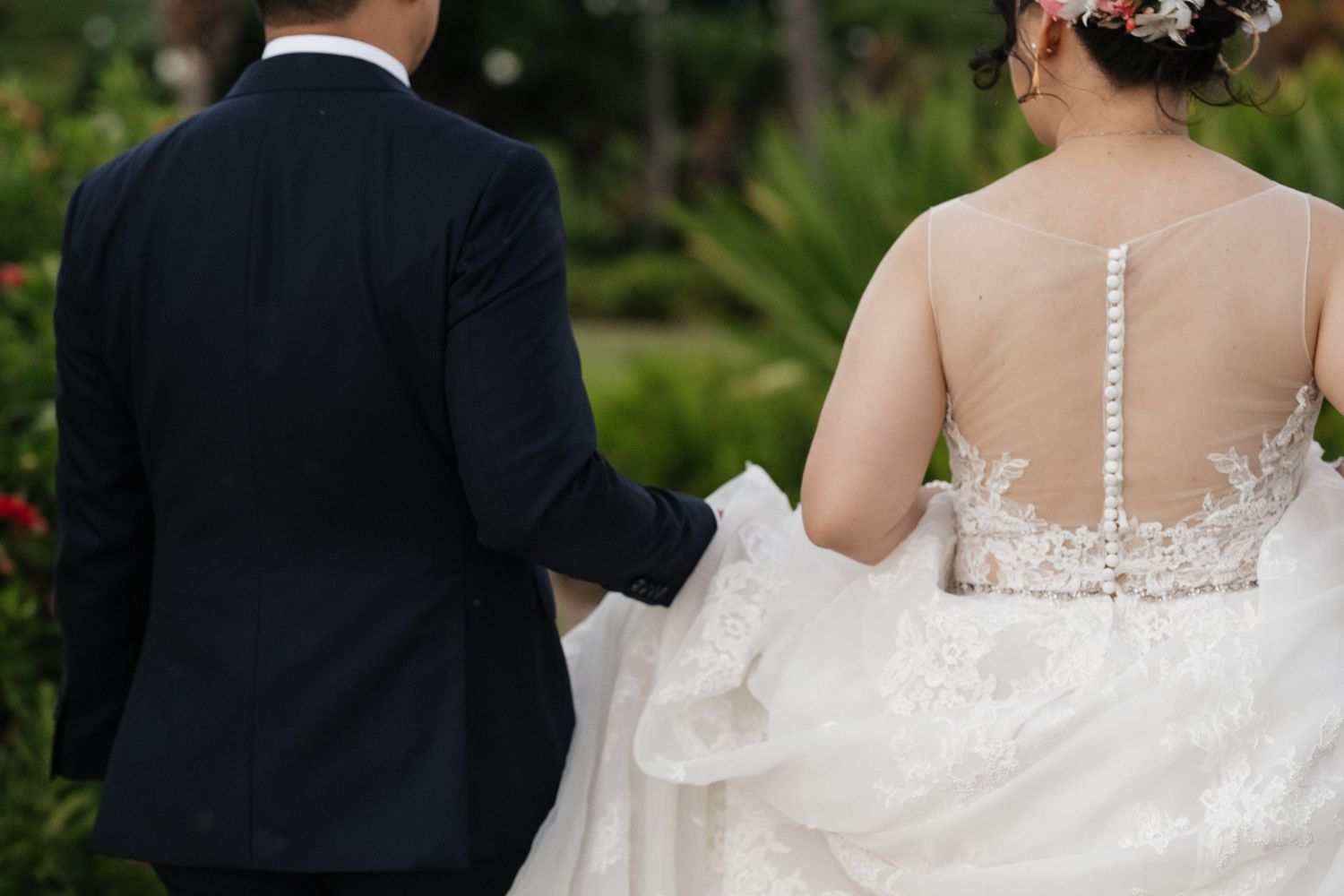 Wedding couple photographed from behind showing intricate lace details of bridal gown.
