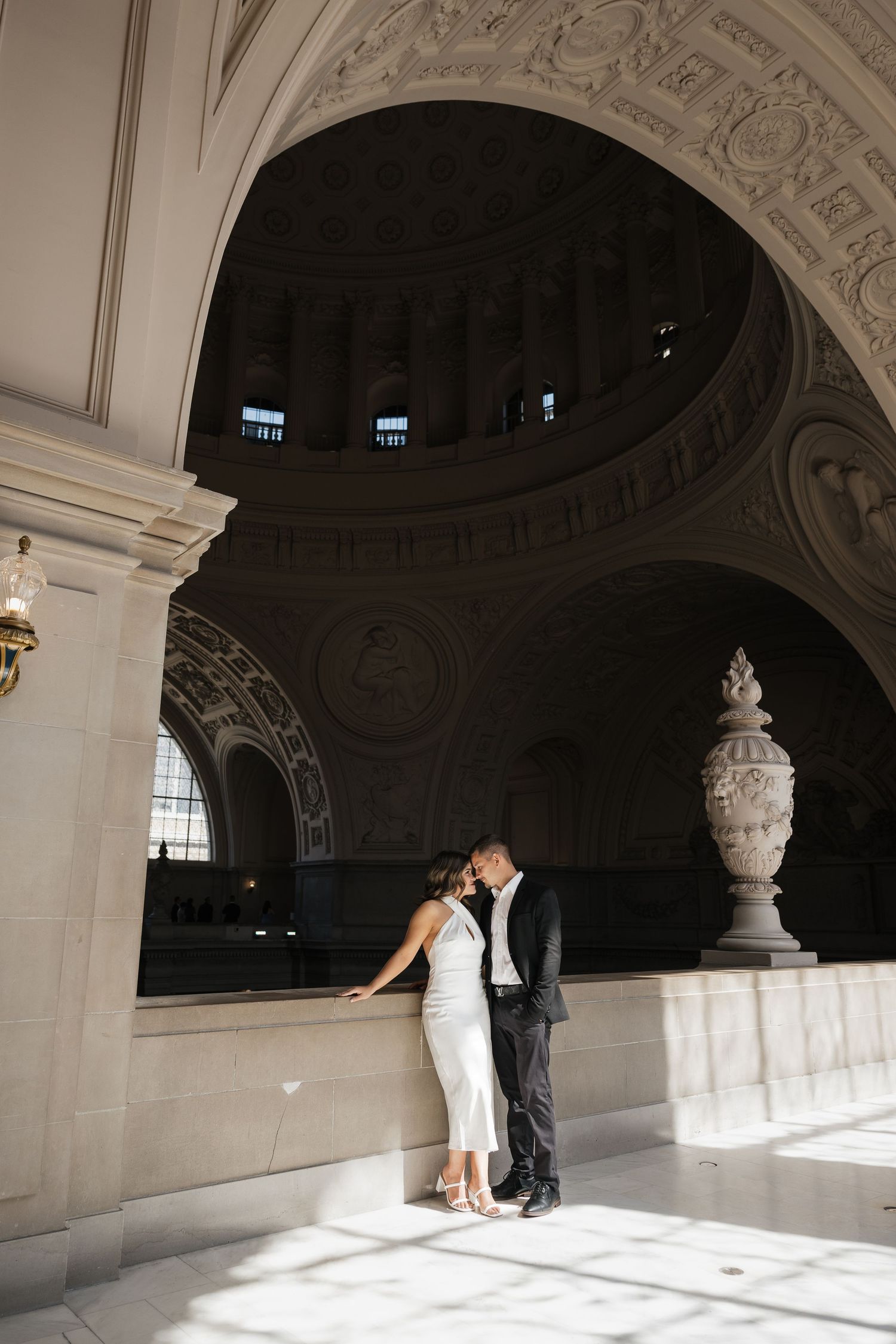 Romantic moment captured under ornate arched ceiling with dramatic natural lighting.