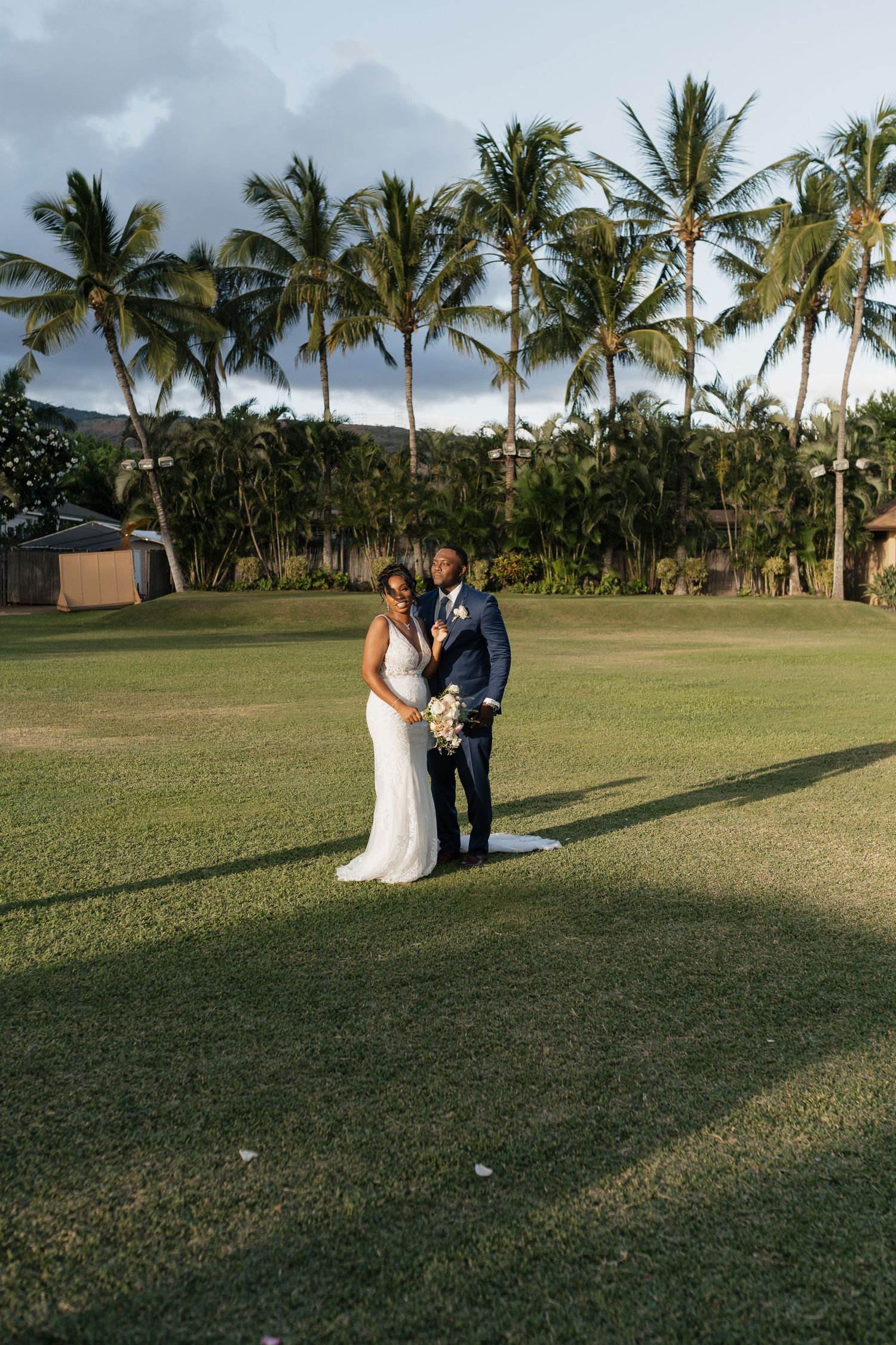 Wedding couple poses for photos on expansive lawn with palm trees at sunset.