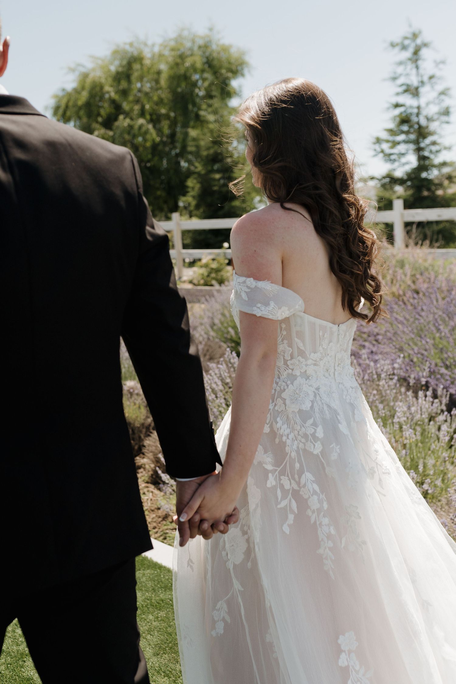 Romantic garden wedding scene with couple walking among lavender flowers.