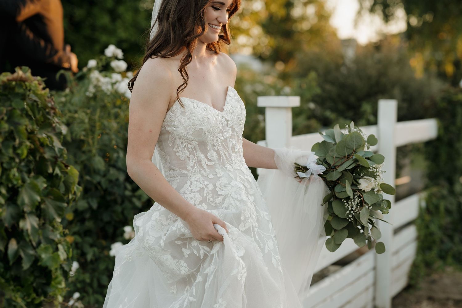 Beautiful white lace wedding dress against a rustic outdoor setting with sunset lighting.