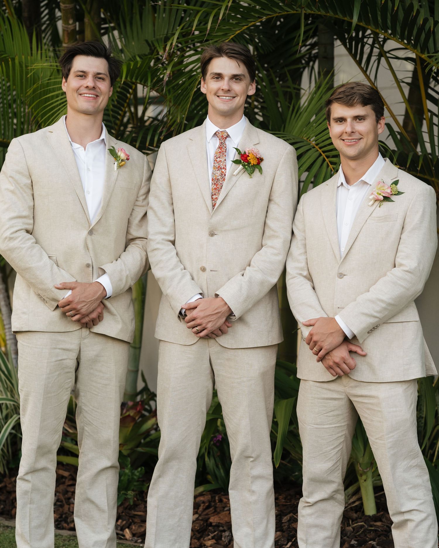 Groomsmen in light beige suits pose together against a tropical garden backdrop.