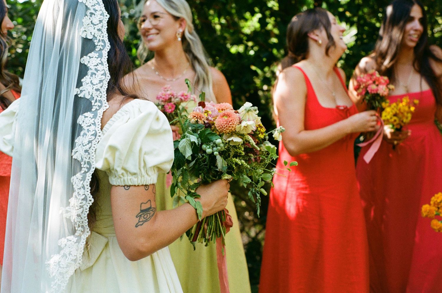 A wedding party poses outdoors in bright red bridesmaid dresses and white bridal gown holding floral bouquets.