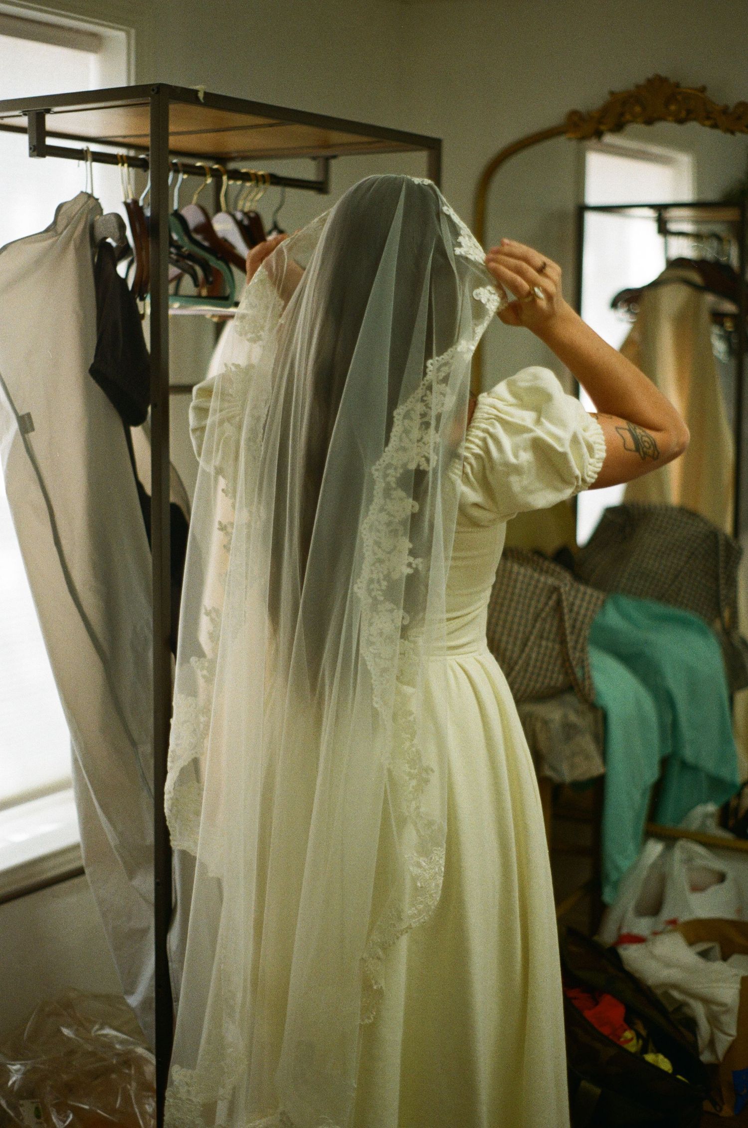 A sequence of white vintage wedding dresses hanging on garment racks in a dimly lit room with soft natural lighting.