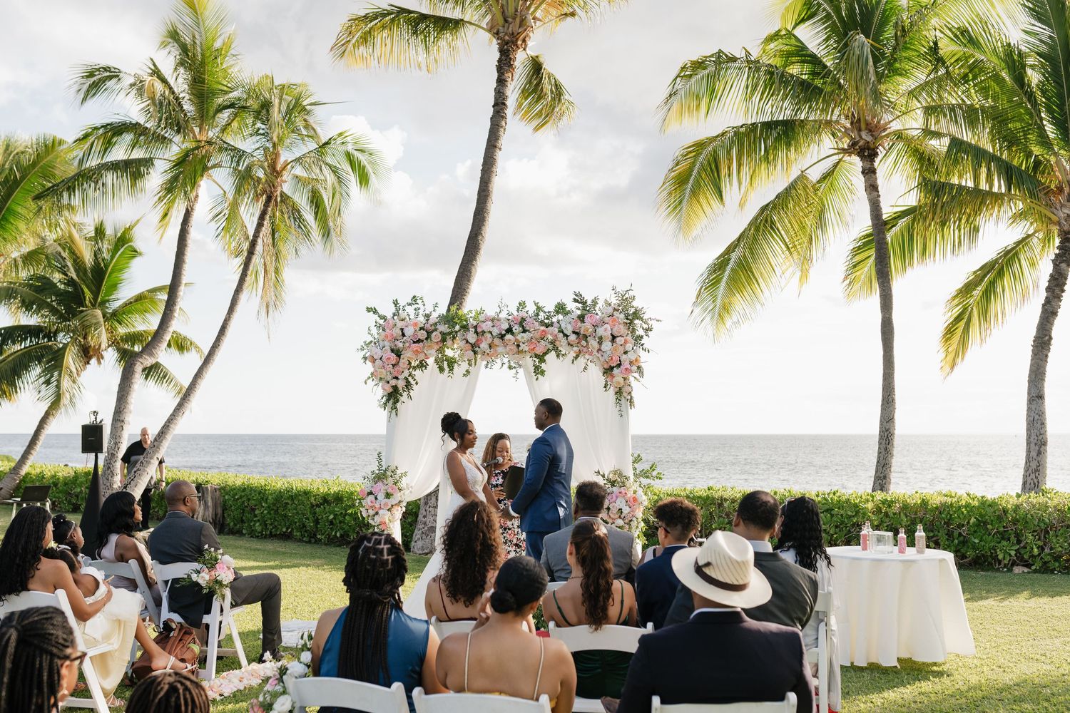 Scenic outdoor wedding reception setup with palm trees and ocean view.