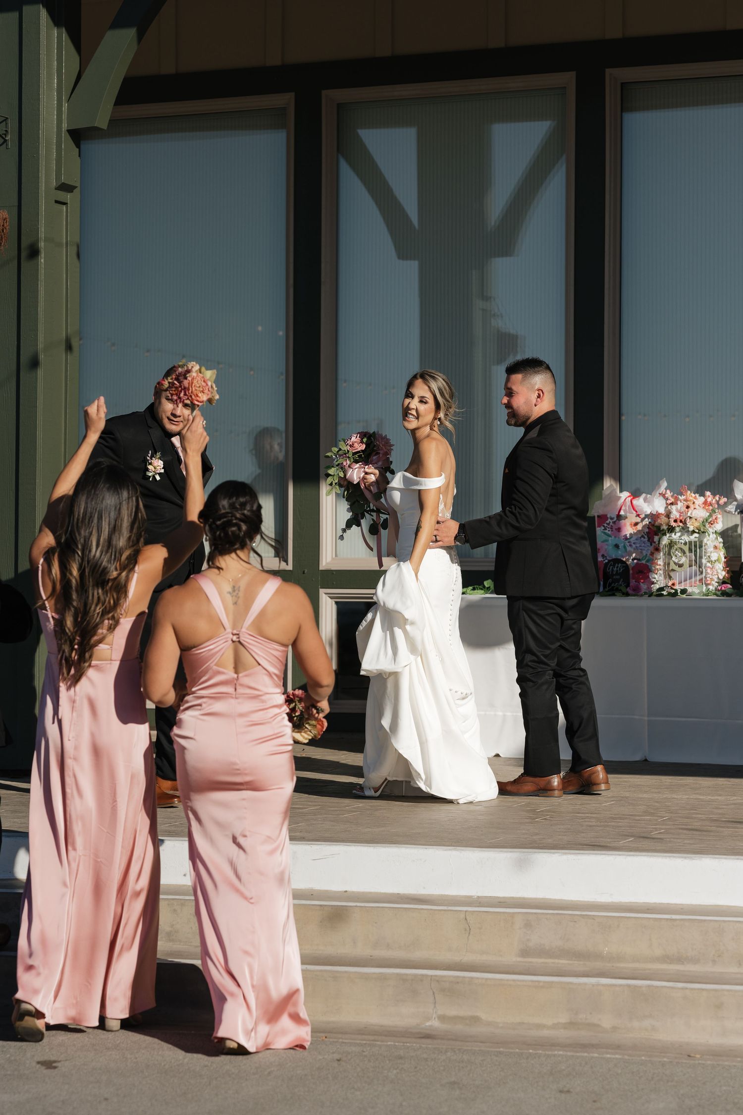 Wedding party in pink dresses watching celebration through glass windows.