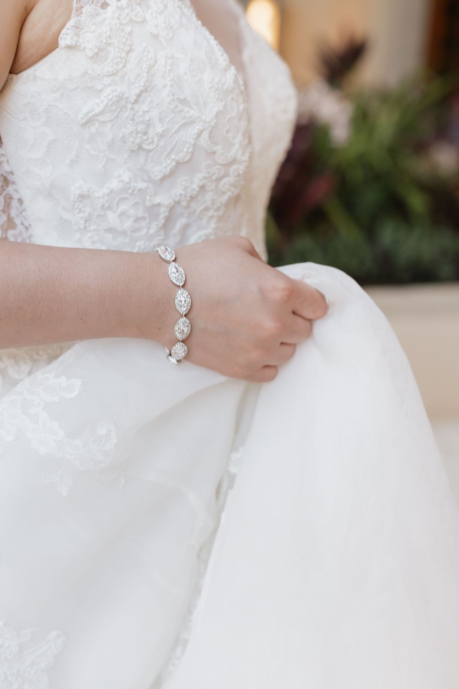 Close-up detail of a bride's delicate bracelet and lace wedding dress.