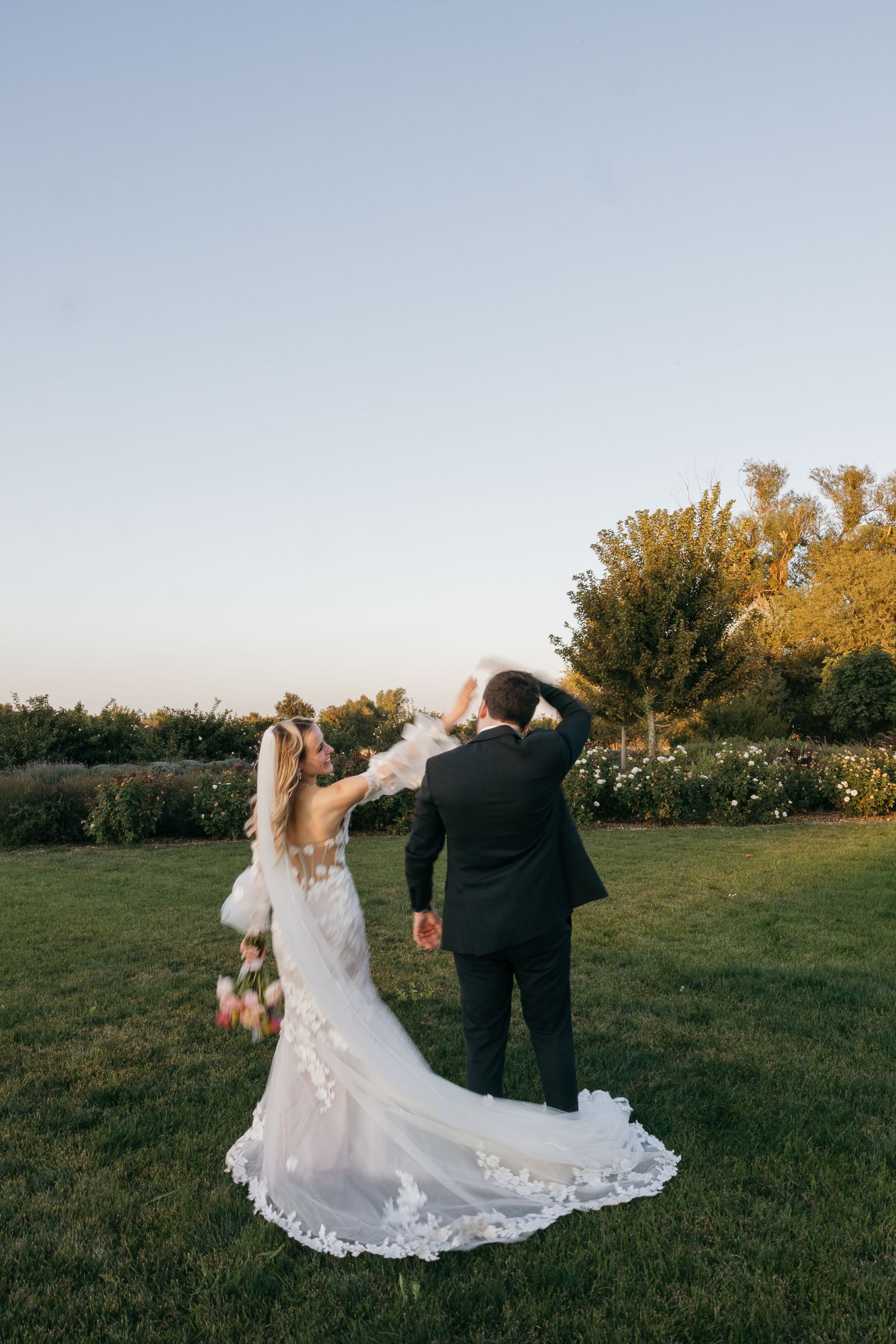 Wedding couple dancing together on lawn during golden hour sunset.