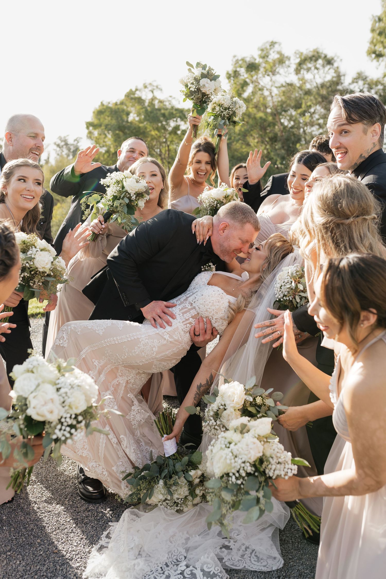 Wedding party celebrates joyfully with arms raised and bouquets in hand.