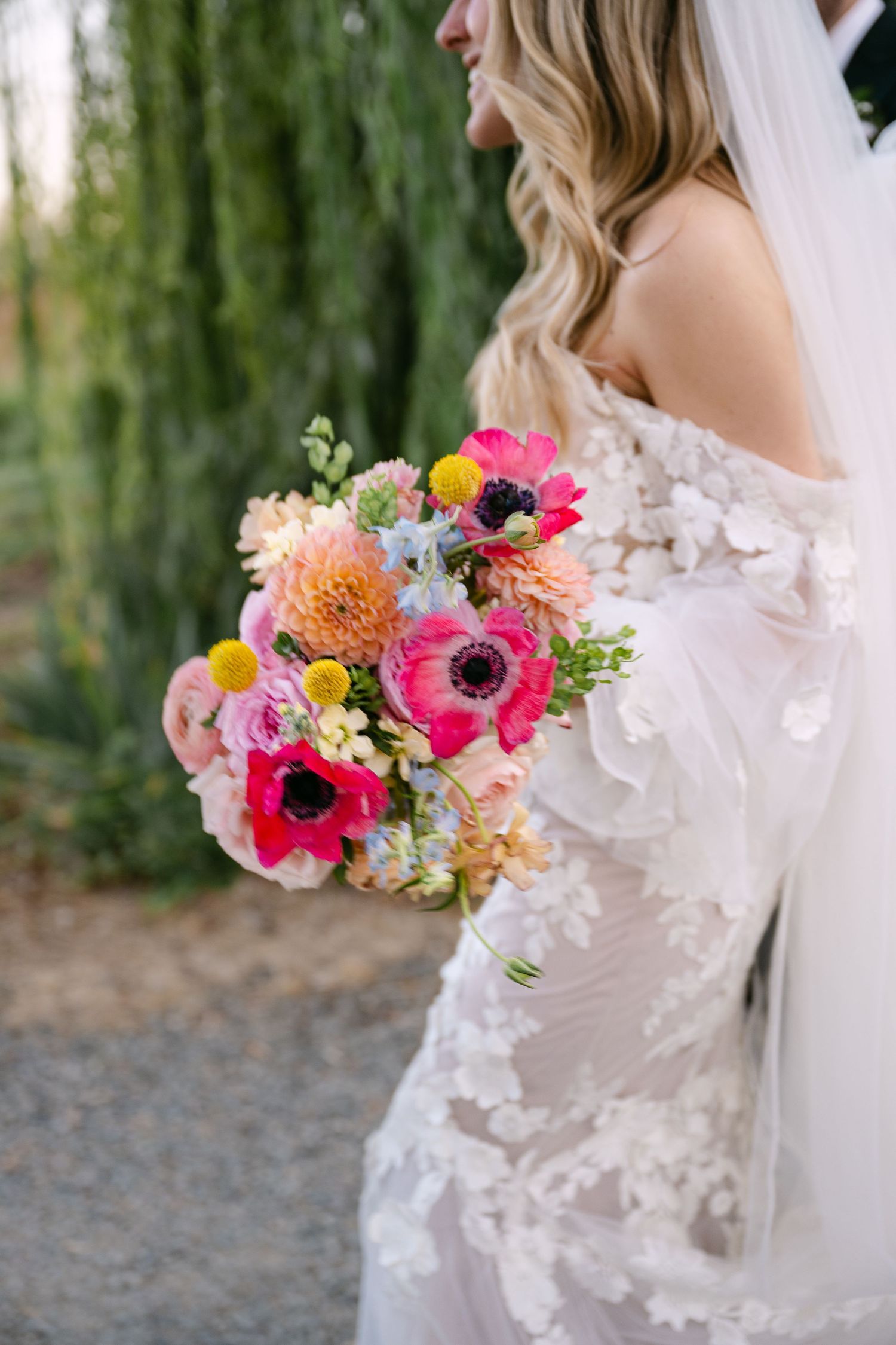 A vibrant pink and coral wedding bouquet with mixed flowers against a soft outdoor background.