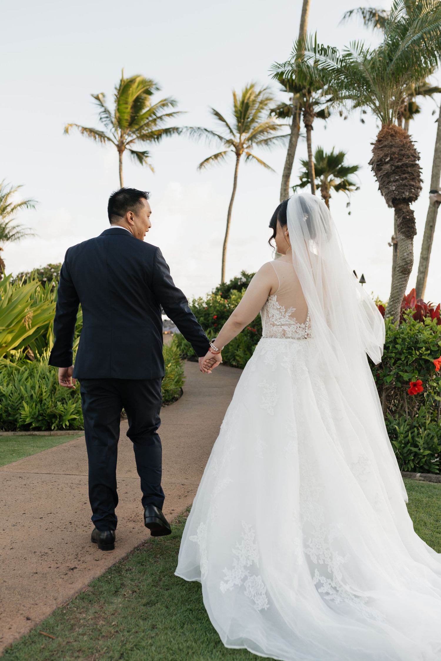 Couple walks along a palm-lined pathway during their tropical wedding photoshoot.