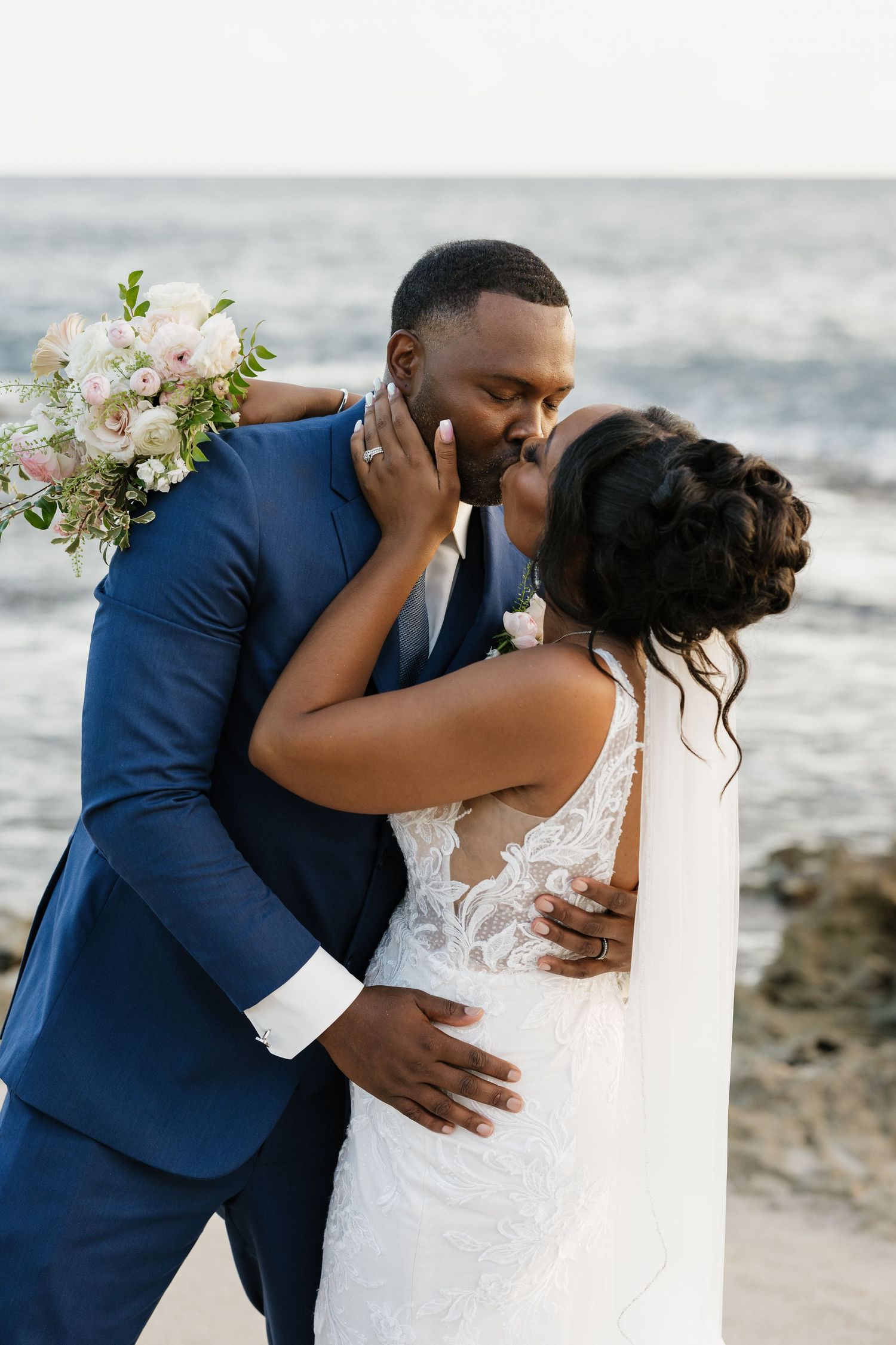 Romantic beach wedding photoshoot with couple embracing against ocean backdrop.