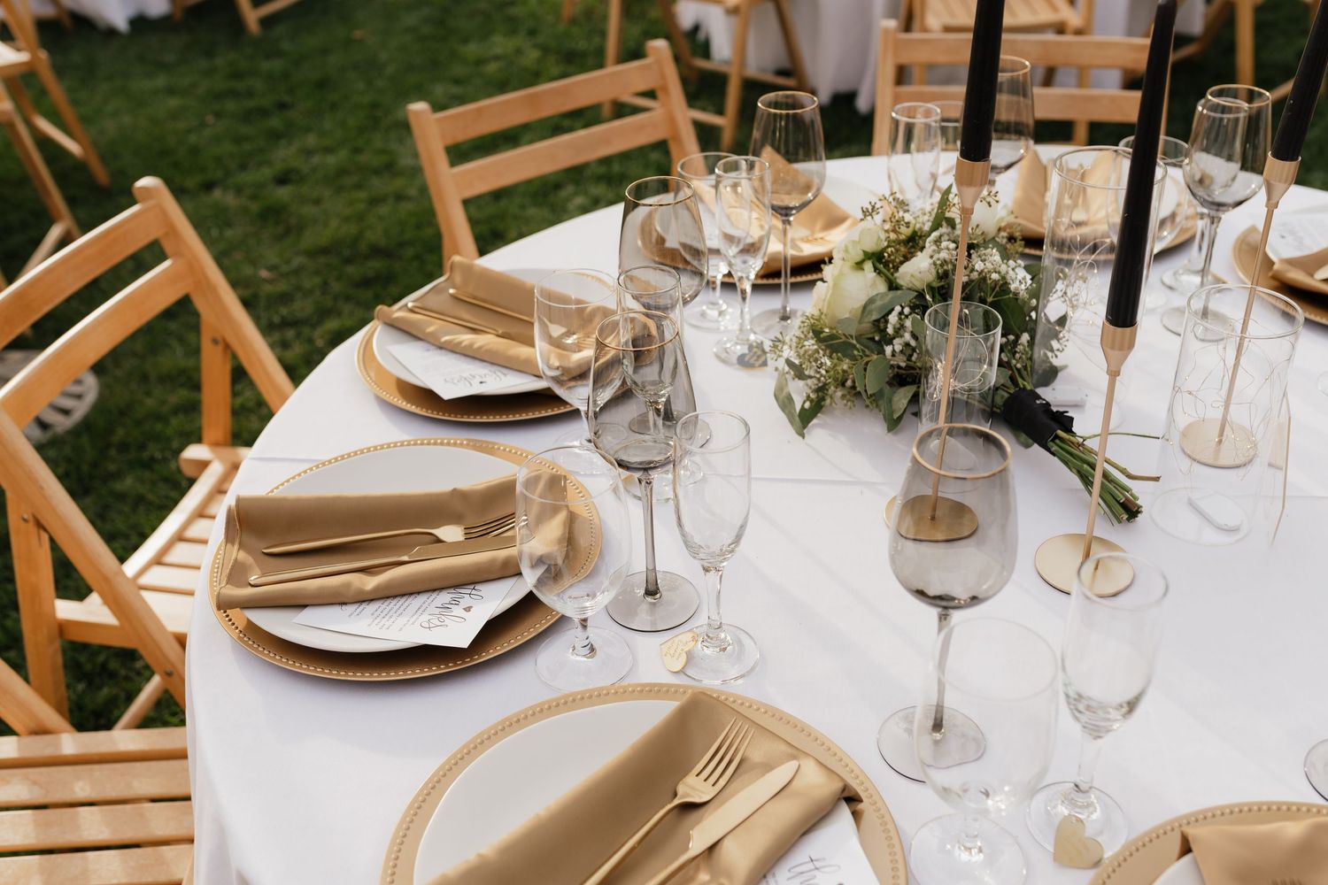 Elegant wedding reception table settings with natural wood chairs, white linens, and delicate floral centerpieces.
