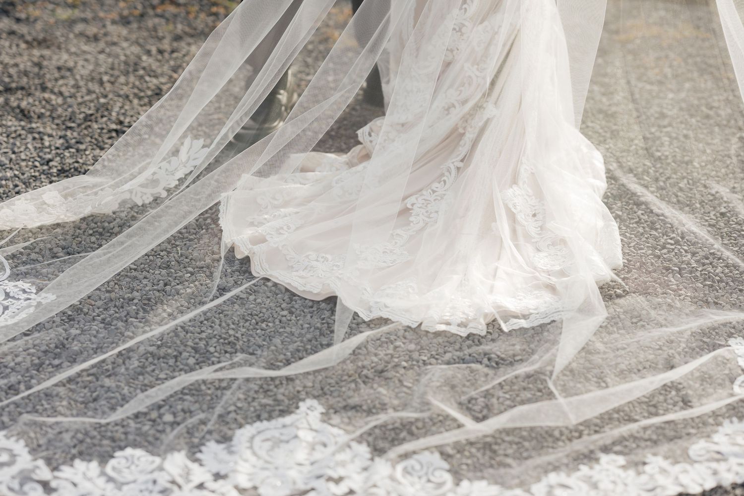 Long flowing bridal veil trailing dramatically on gravel path.