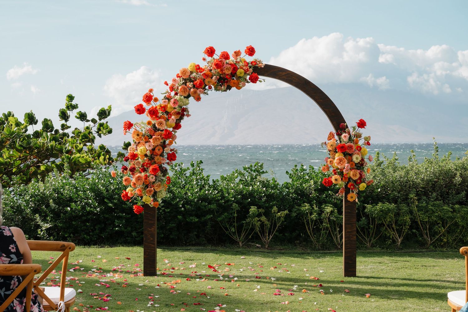 Wedding arch decorated with vibrant orange flowers overlooking a scenic countryside landscape.
