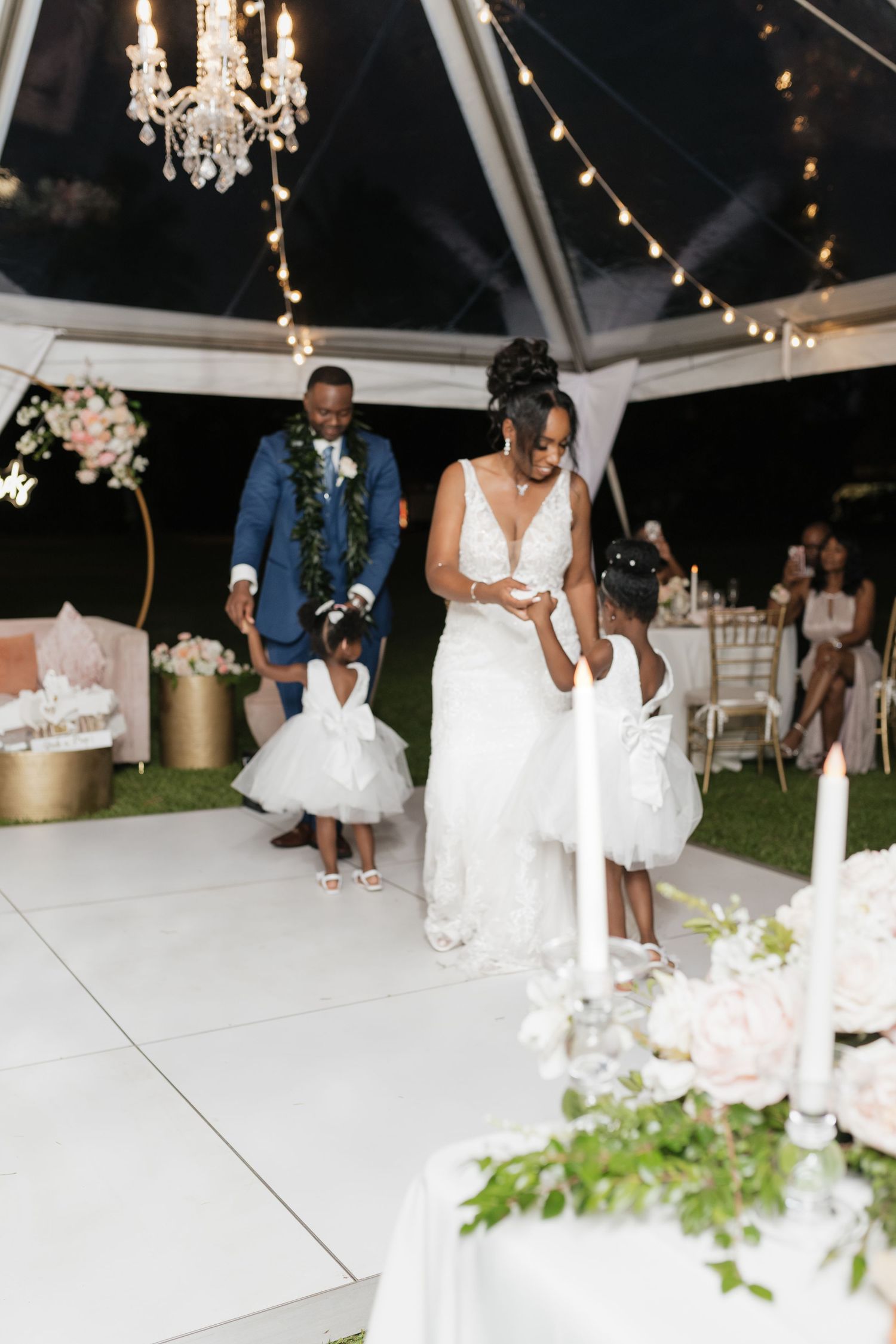 White dance floor and elegant table settings under a tent with string lights at an outdoor wedding.